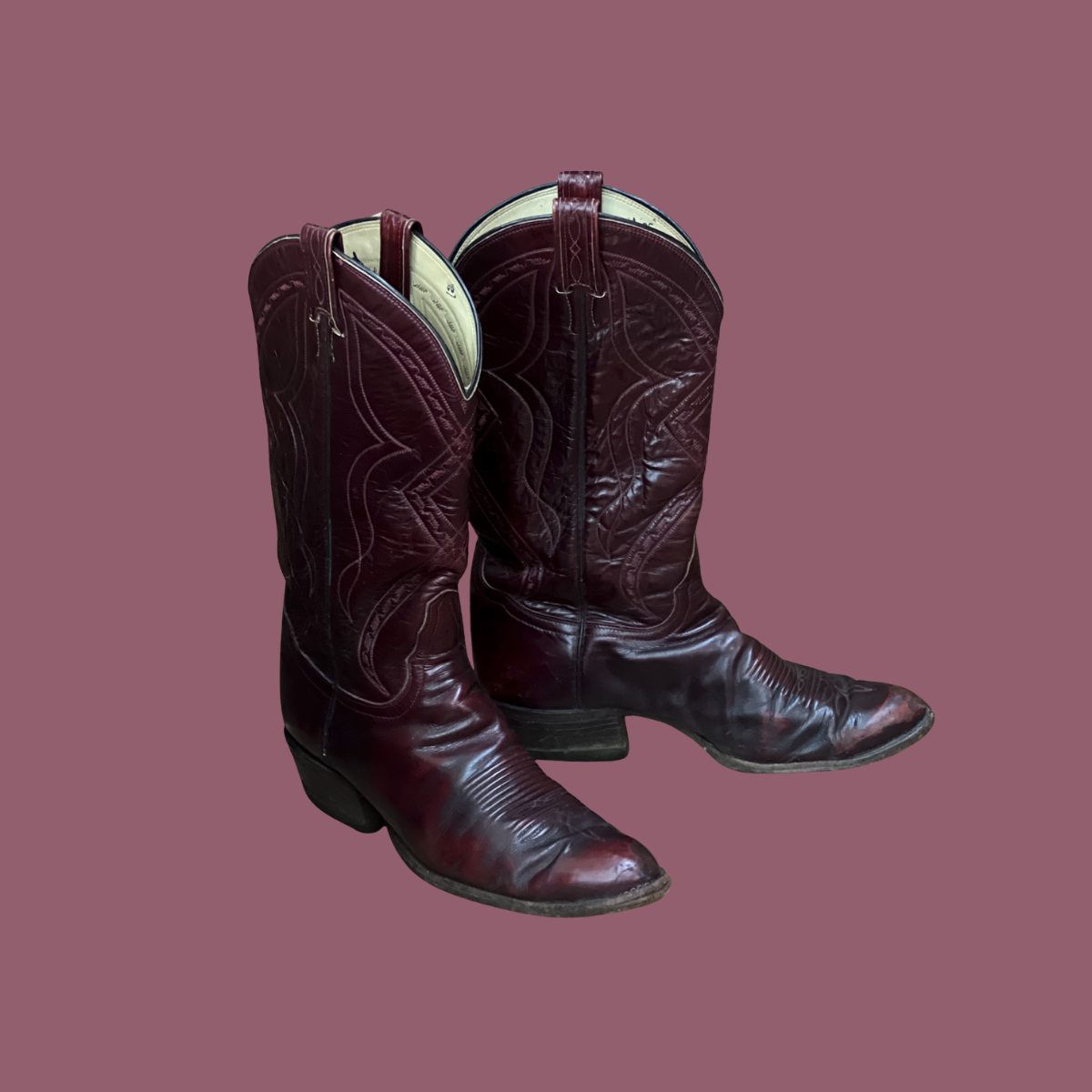 A pair of dark red cowboy boots with pointed toes and intricate stitching patterns.