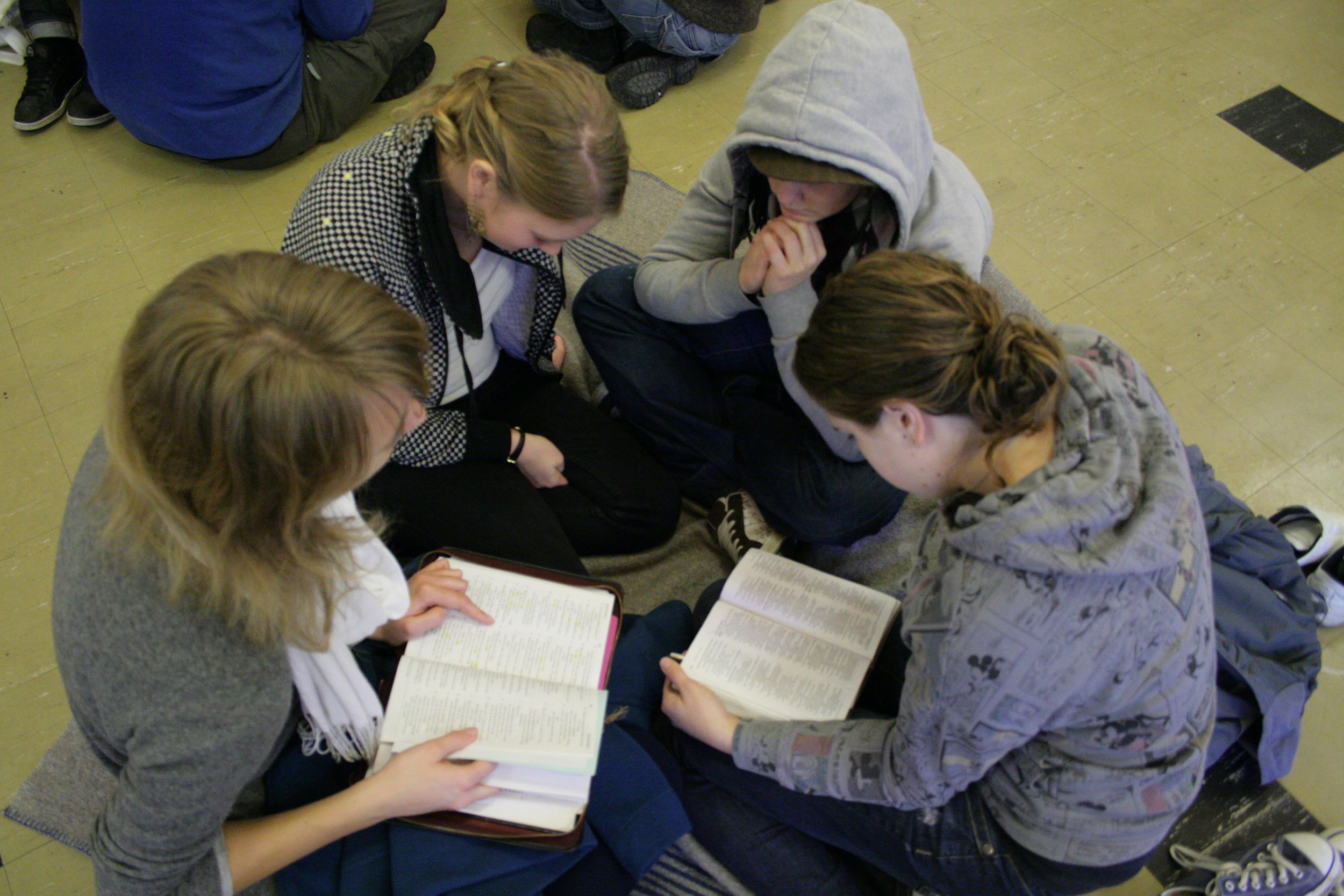 Group of five young women sitting in a circle on the floor, reading books together.