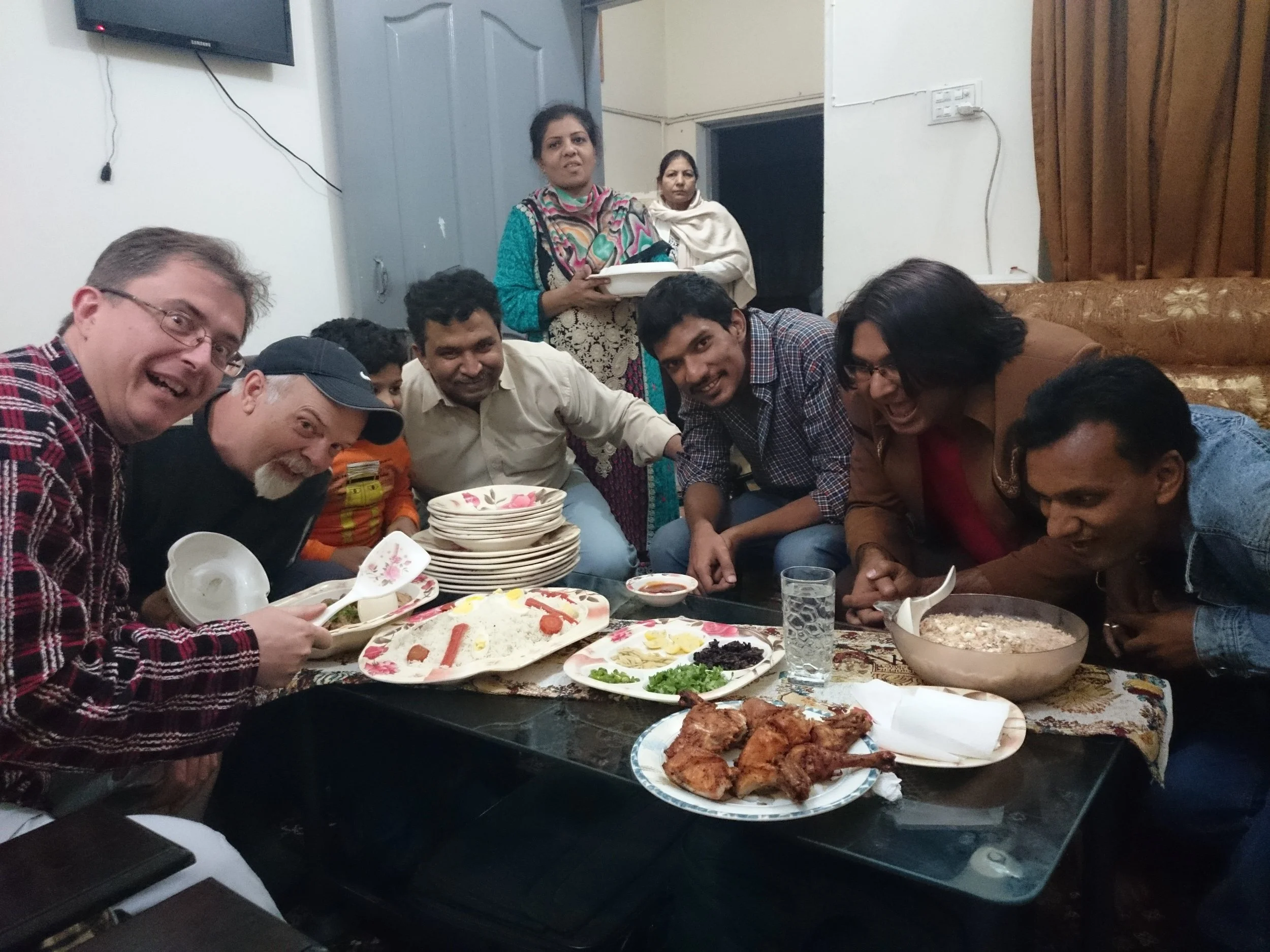Group of people gathered around a table with food, smiling and posing for a photo during a celebration or gathering.