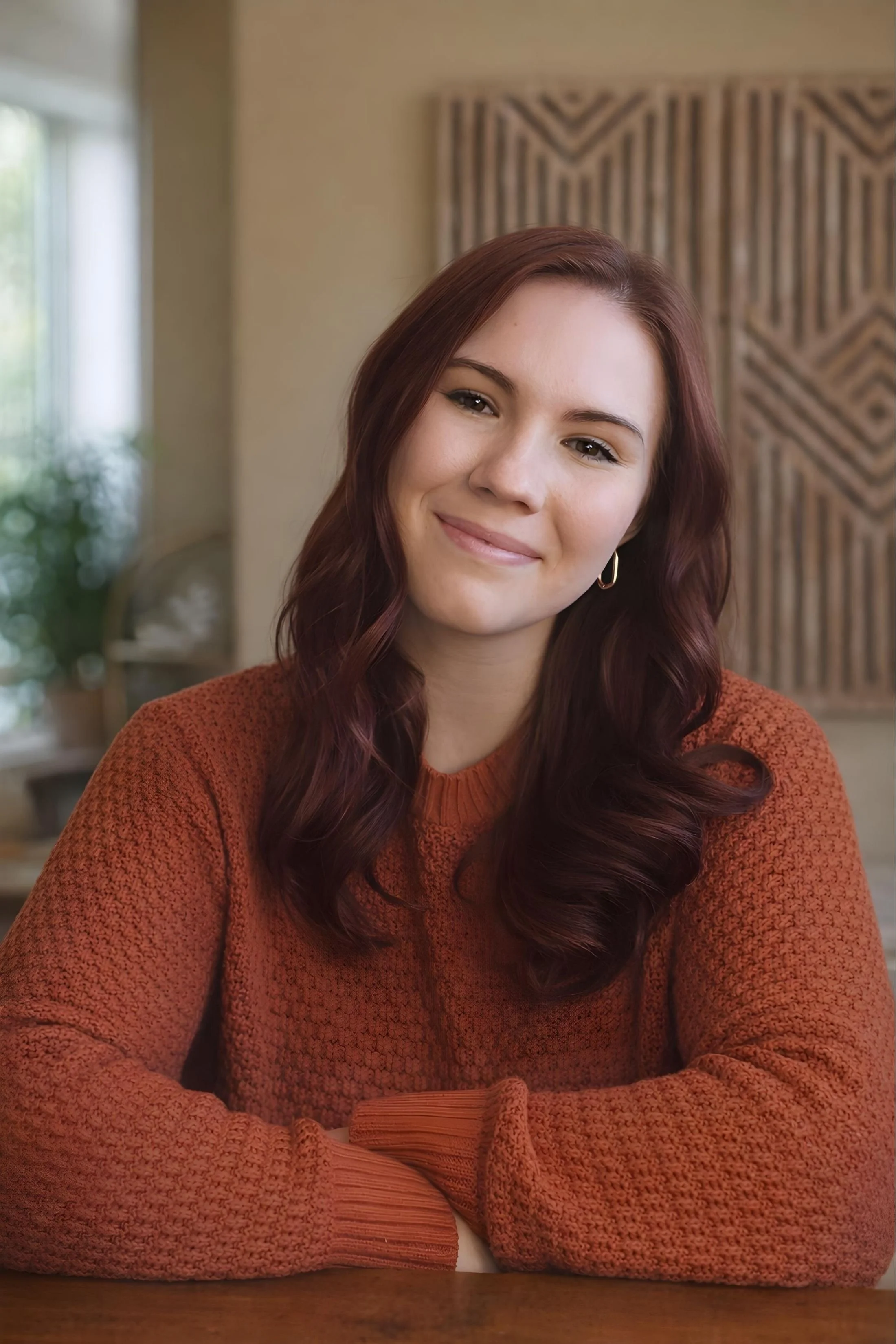 Young woman therapist with auburn hair sitting in a relaxed pose with arms crossed and a soft smile