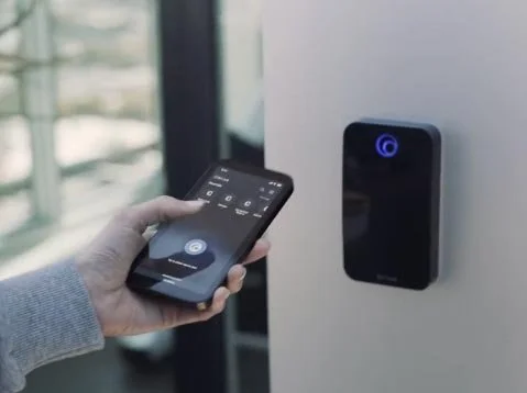 Person holding a smartphone near a door access keypad.