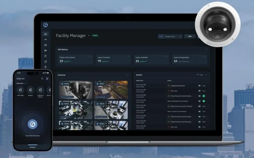 A laptop screen displaying a facility management dashboard with KPIs, camera feeds, and event logs, a smartphone showing a security app, and a security camera in the background over a cityscape.