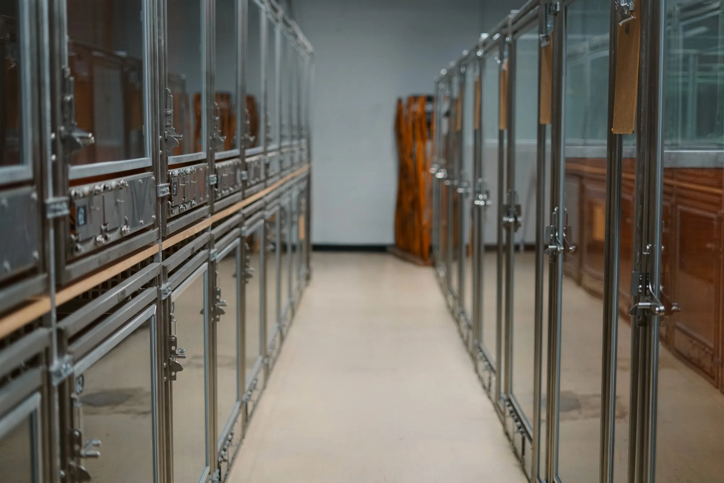 An aisle in a furniture or hardware store with metal shelving units on both sides, some holding glass display cases and others made of wood, extending into the distance.