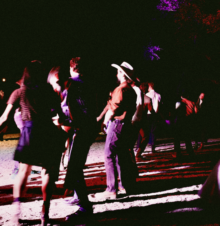People holding hands and dancing outdoors at night under illuminated trees.