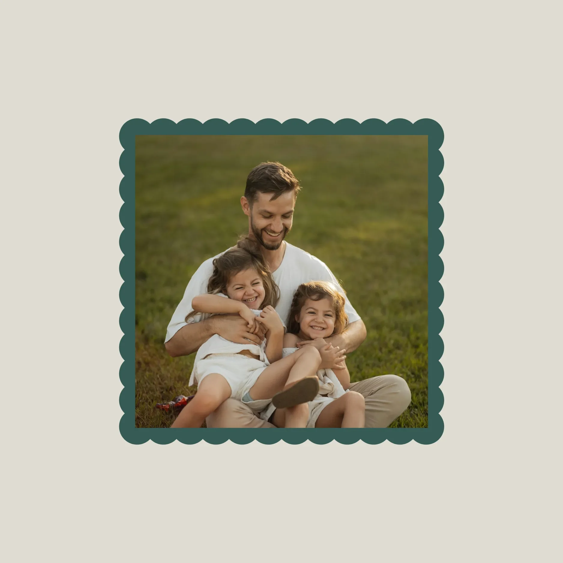 A dad sitting on grass with two young daughters, all smiling and hugging each other.