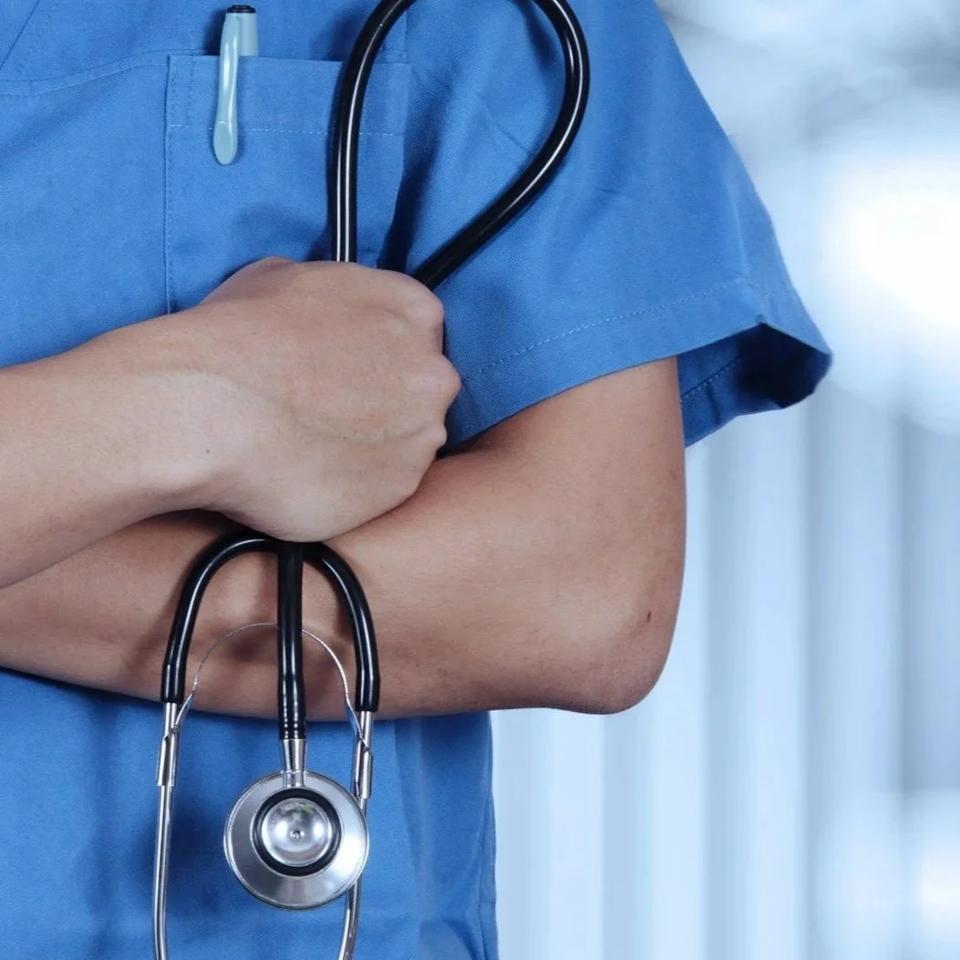 Close-up of a healthcare professional in blue scrubs holding a stethoscope.