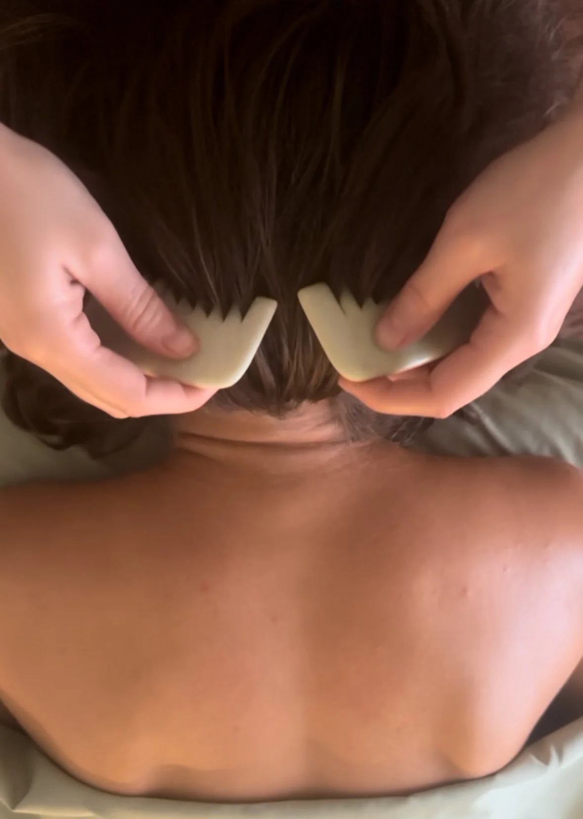 Person lying face down on a massage table receiving a hot stone massage on their back.