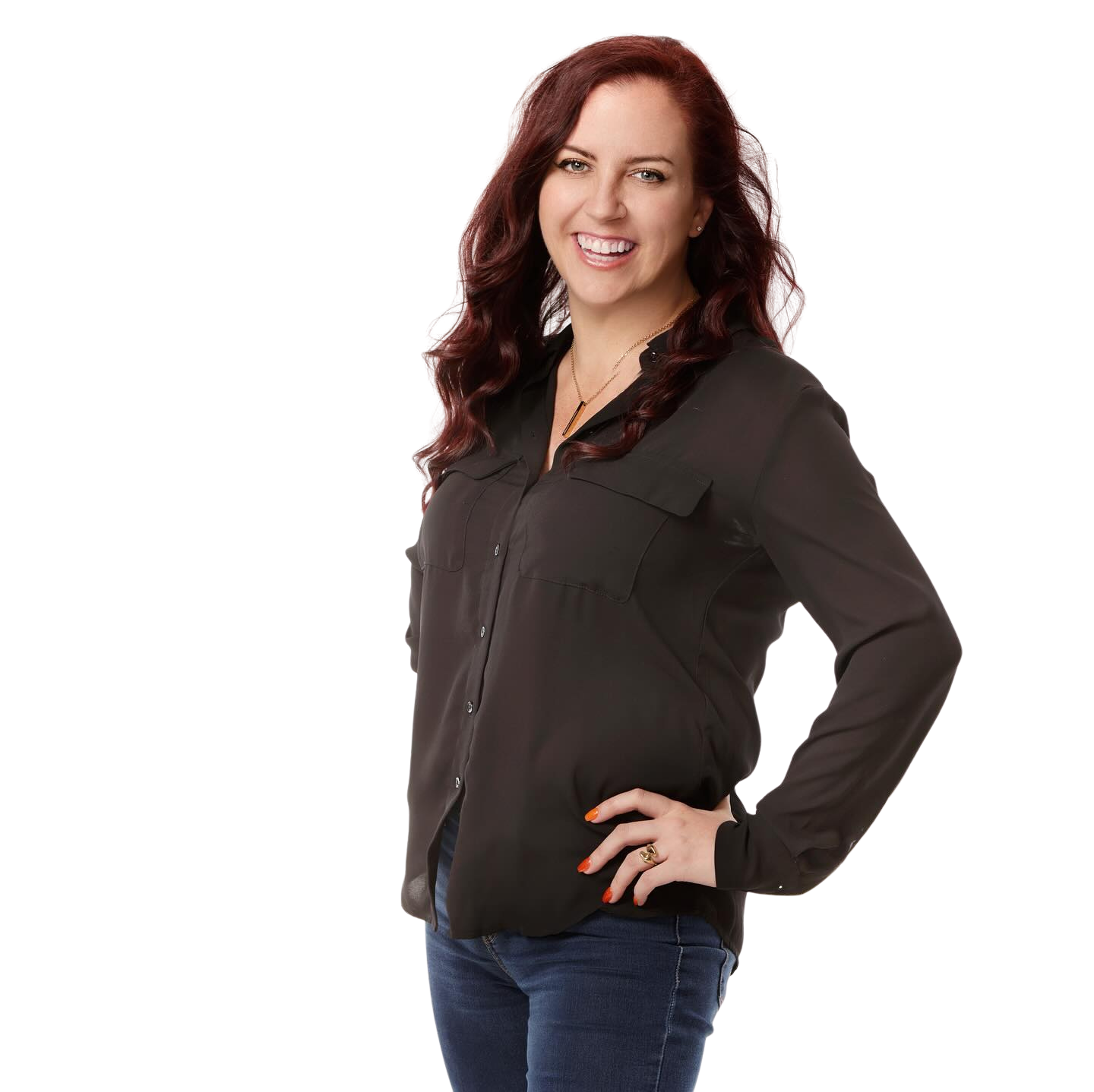 A smiling woman with long, wavy red hair wearing a black button-up shirt and blue jeans.