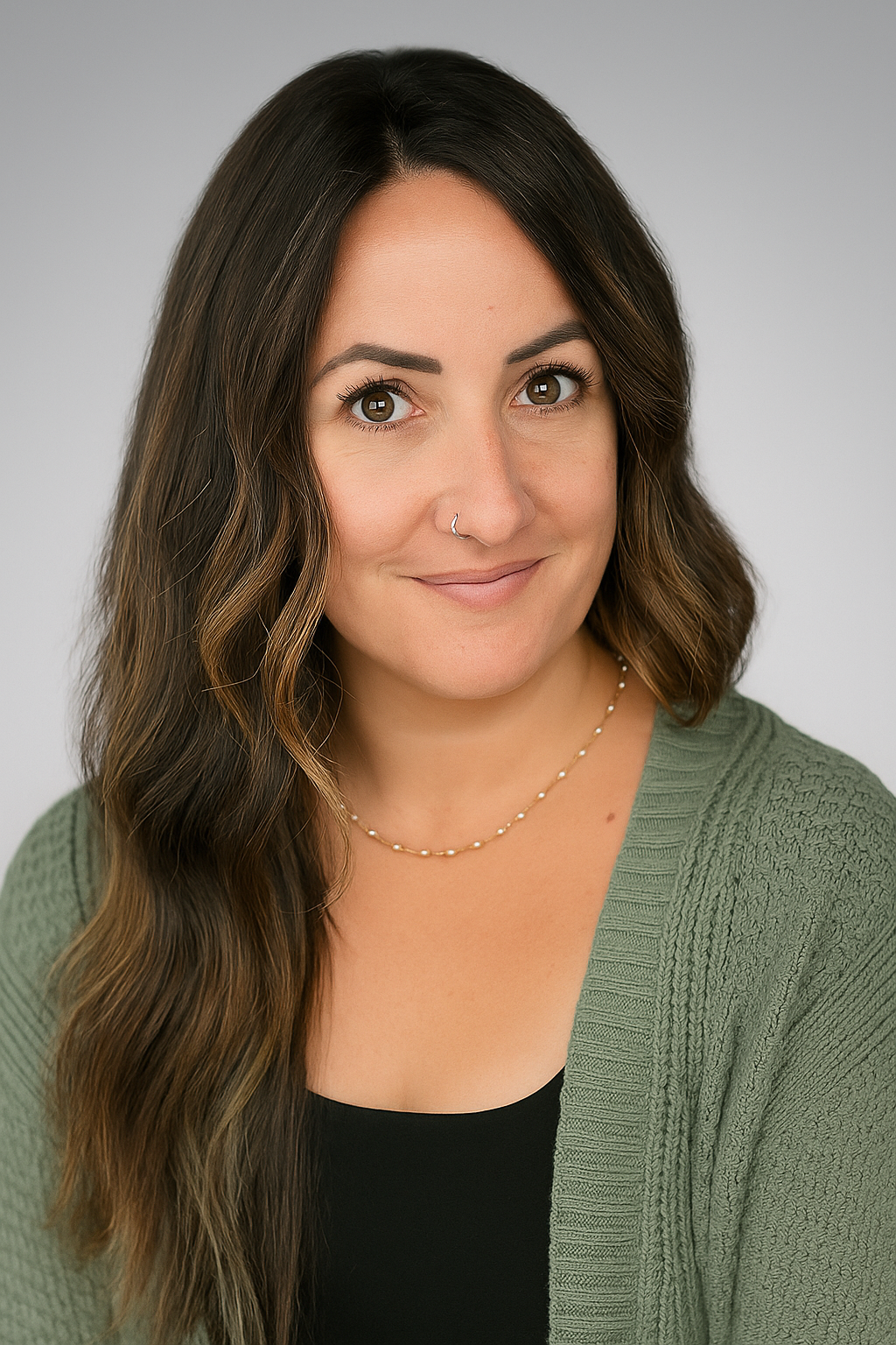 A woman with long wavy brown hair, wearing a green cardigan, black top, and a pearl necklace, smiling against a light gray background.