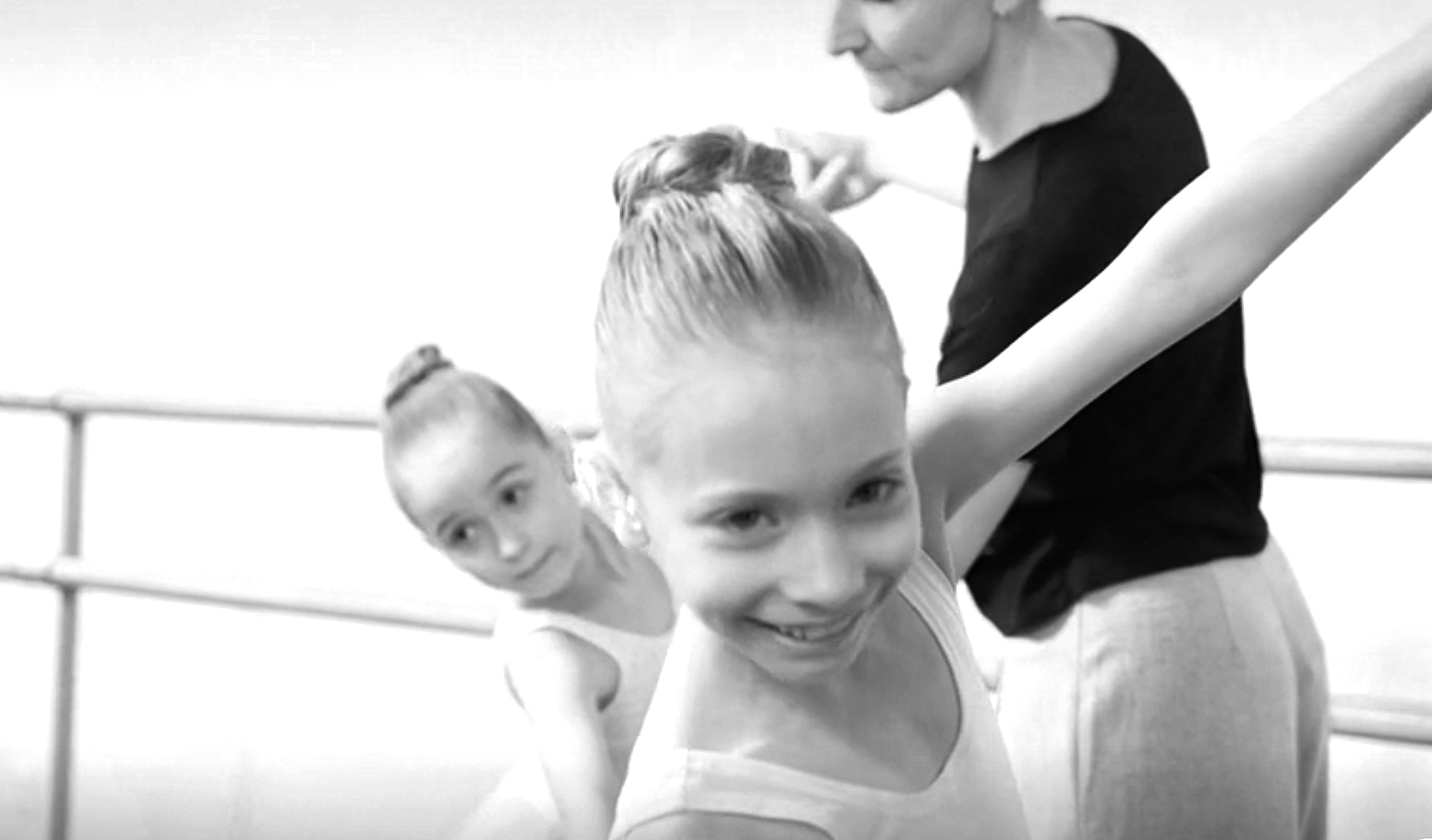 Three young ballet dancers in leotards and an instructor stretching on ballet barres in a dance studio.