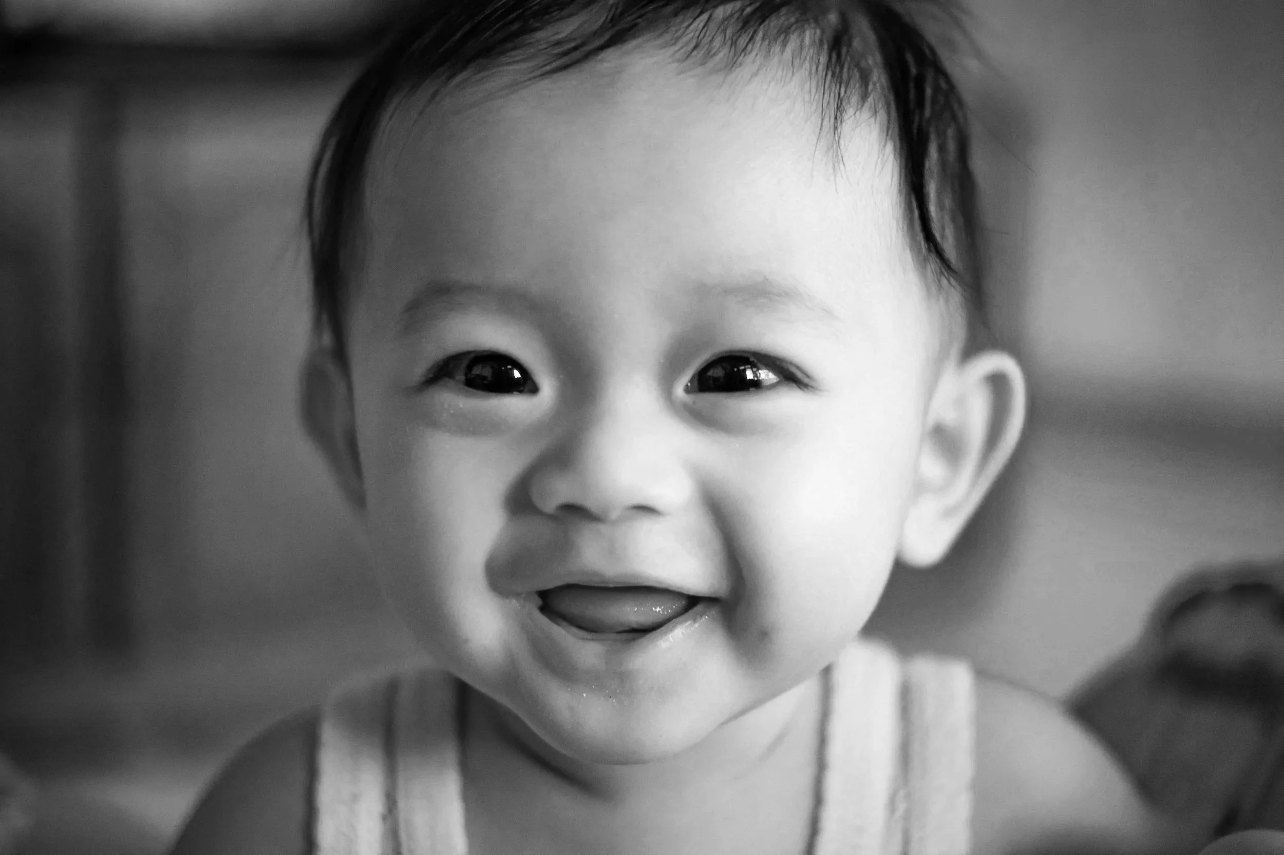 Close-up black and white photo of a smiling baby with short hair, wearing a sleeveless top.