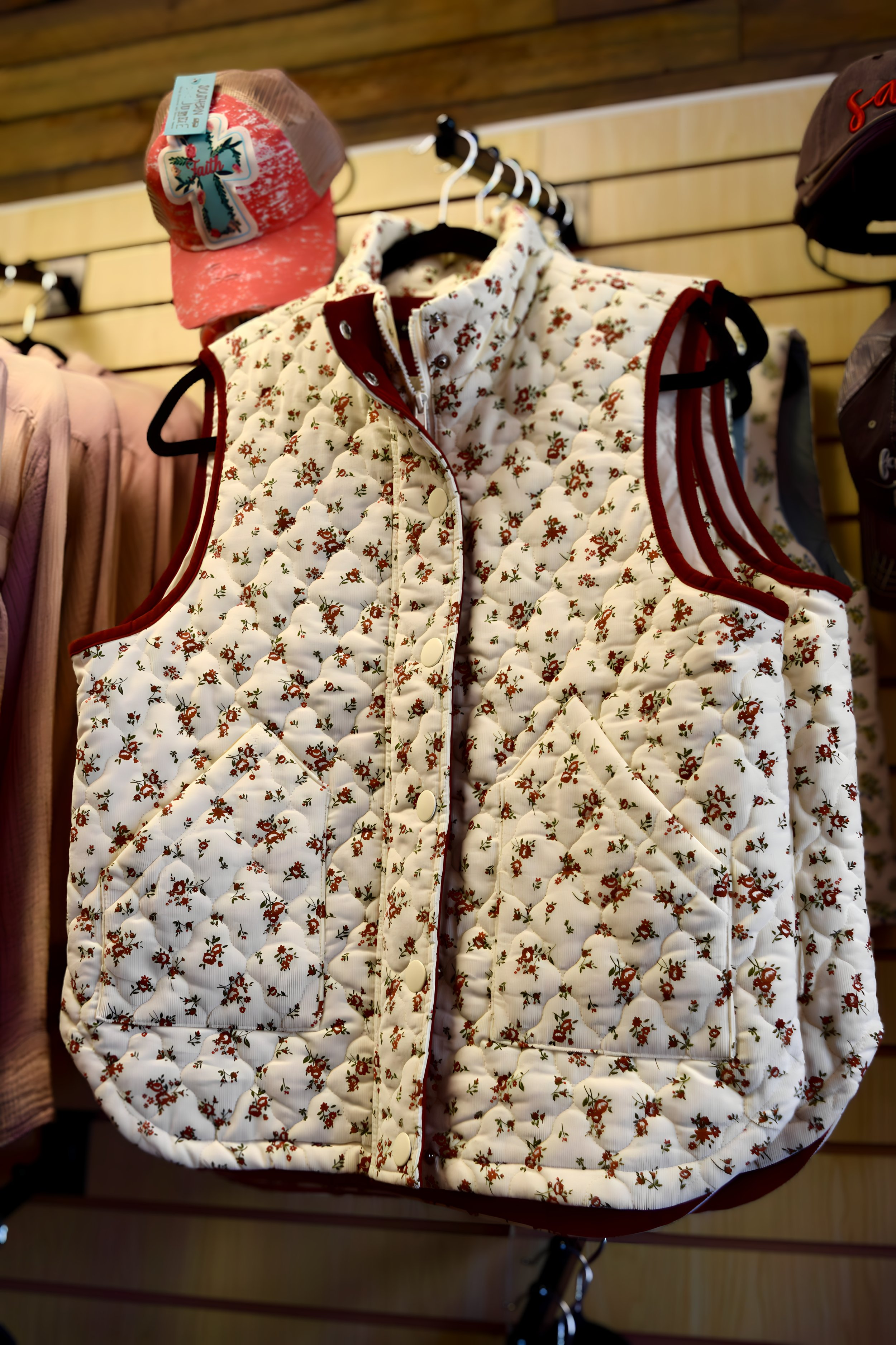 A white quilted vest with a floral pattern displayed on a hanger in a clothing store.