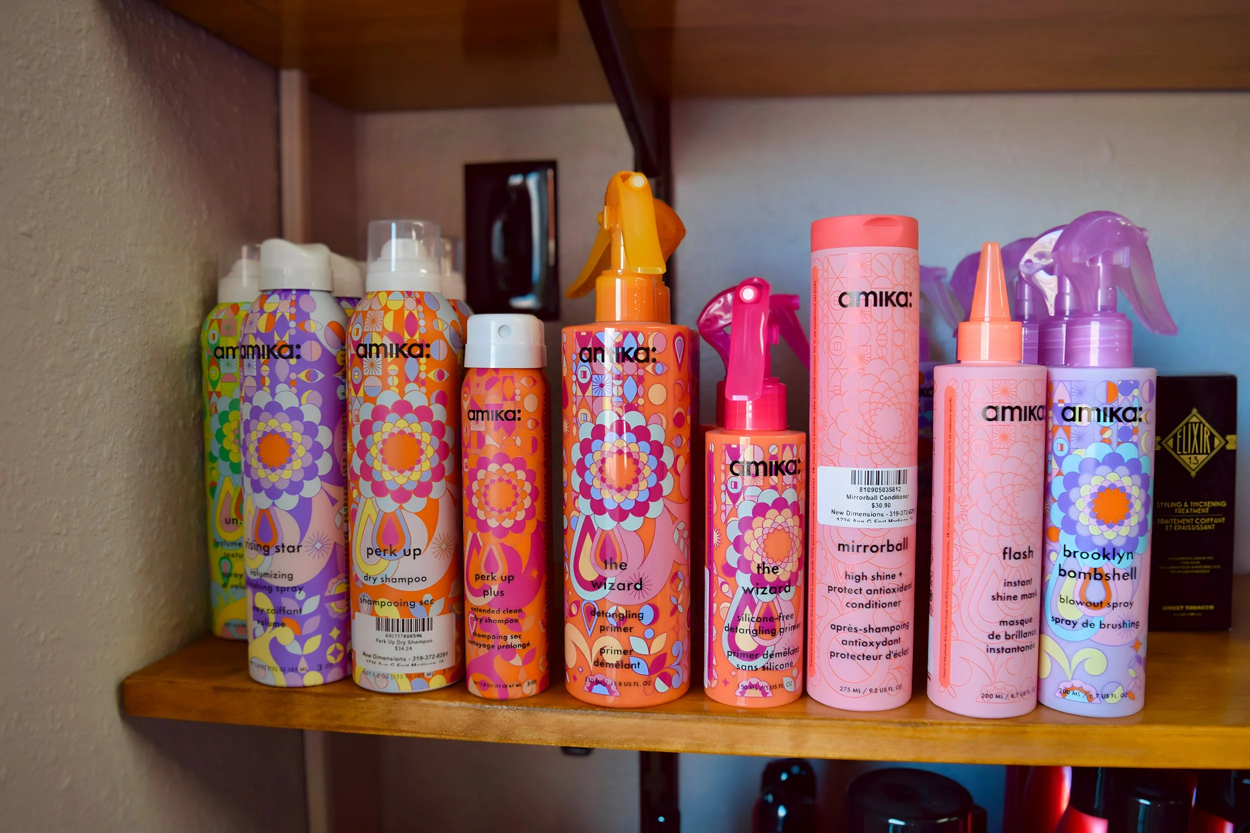 A shelf with colorful bottles of Amika hair products, including shampoo, conditioner, and styling spray, with vibrant floral and geometric designs.