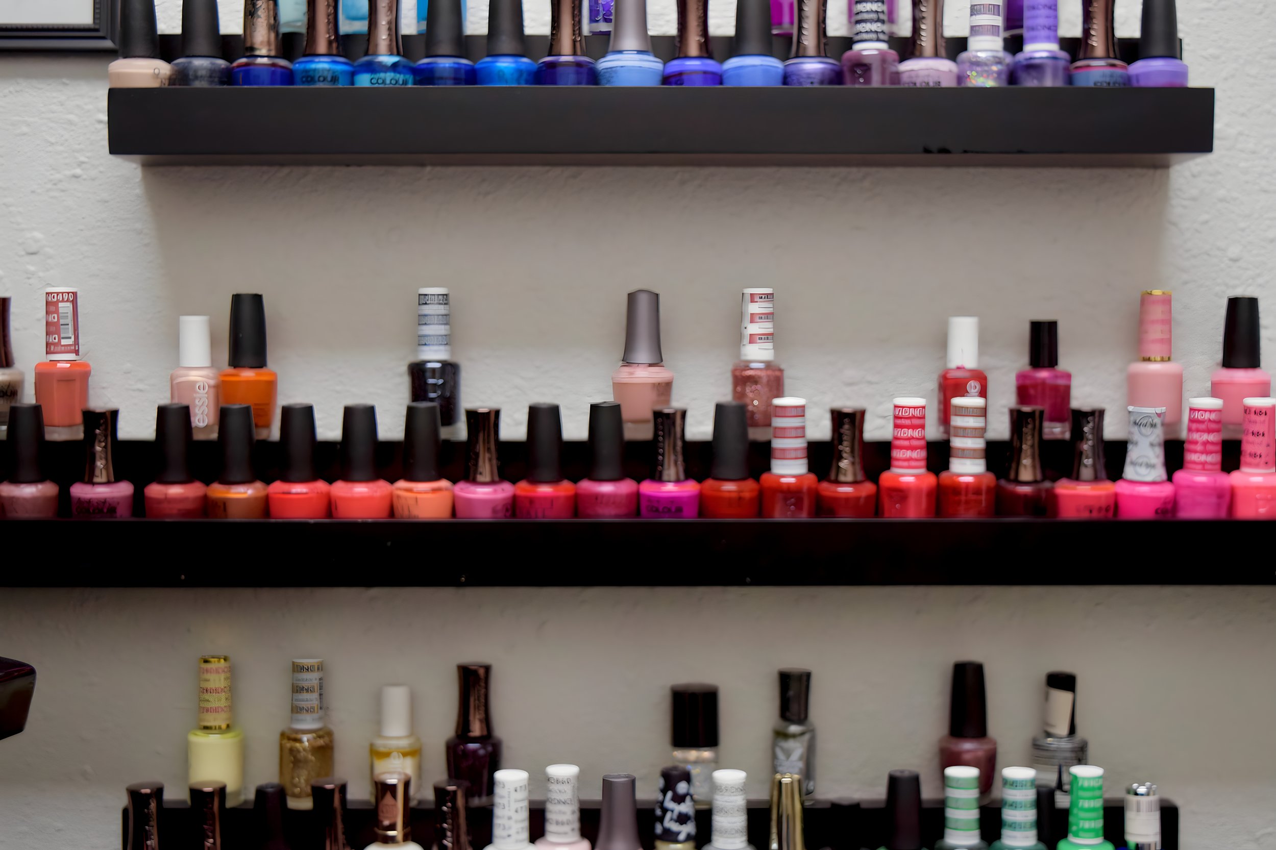 Multiple rows of nail polish bottles in various colors on black shelves.