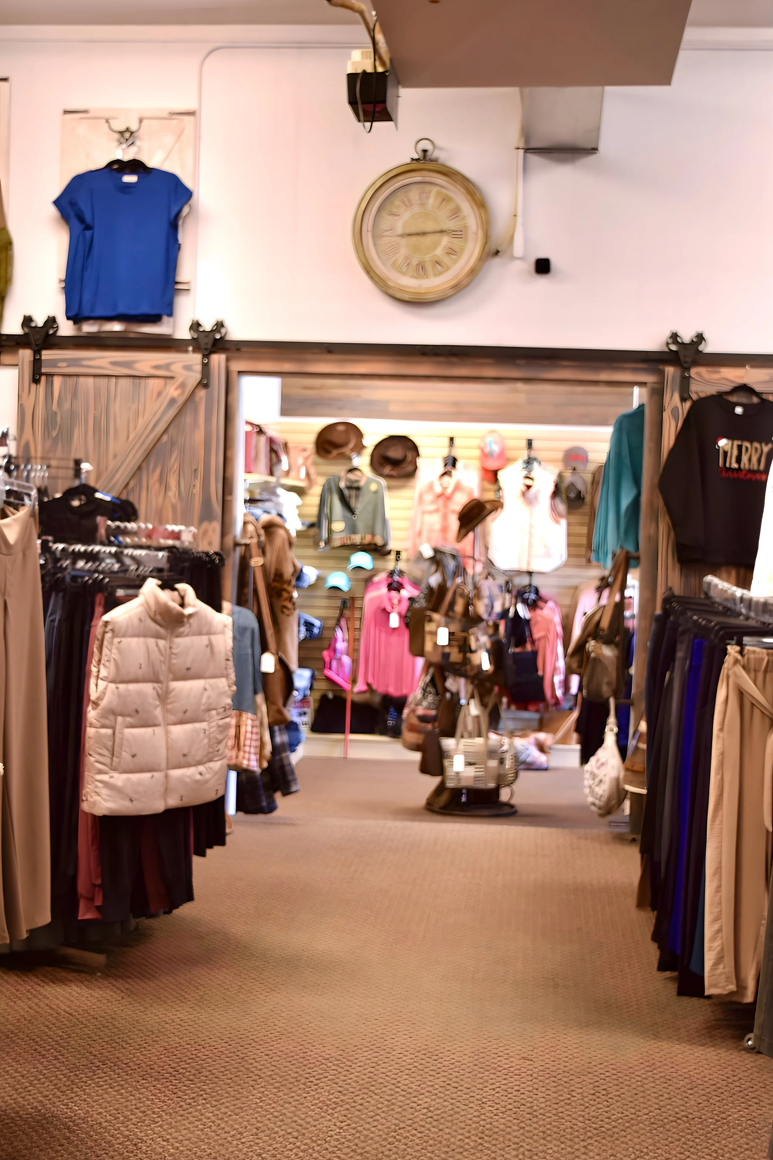 View of a clothing store with racks of pants, dresses, hats, and jackets. A large clock on the wall shows 11:55.