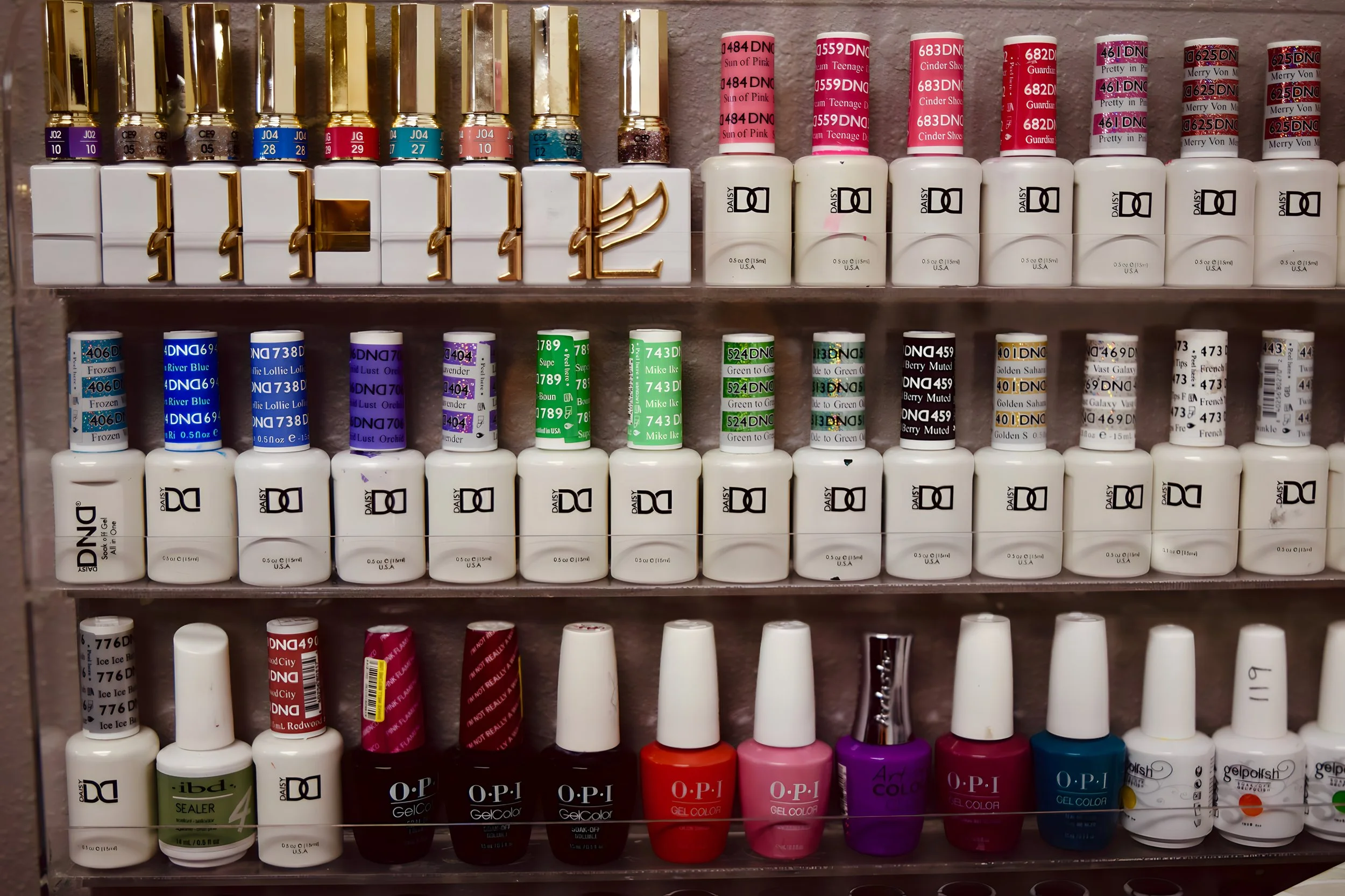 Display of various nail polish bottles arranged on clear shelves, including different brands and colors such as pink, blue, purple, red, and white.