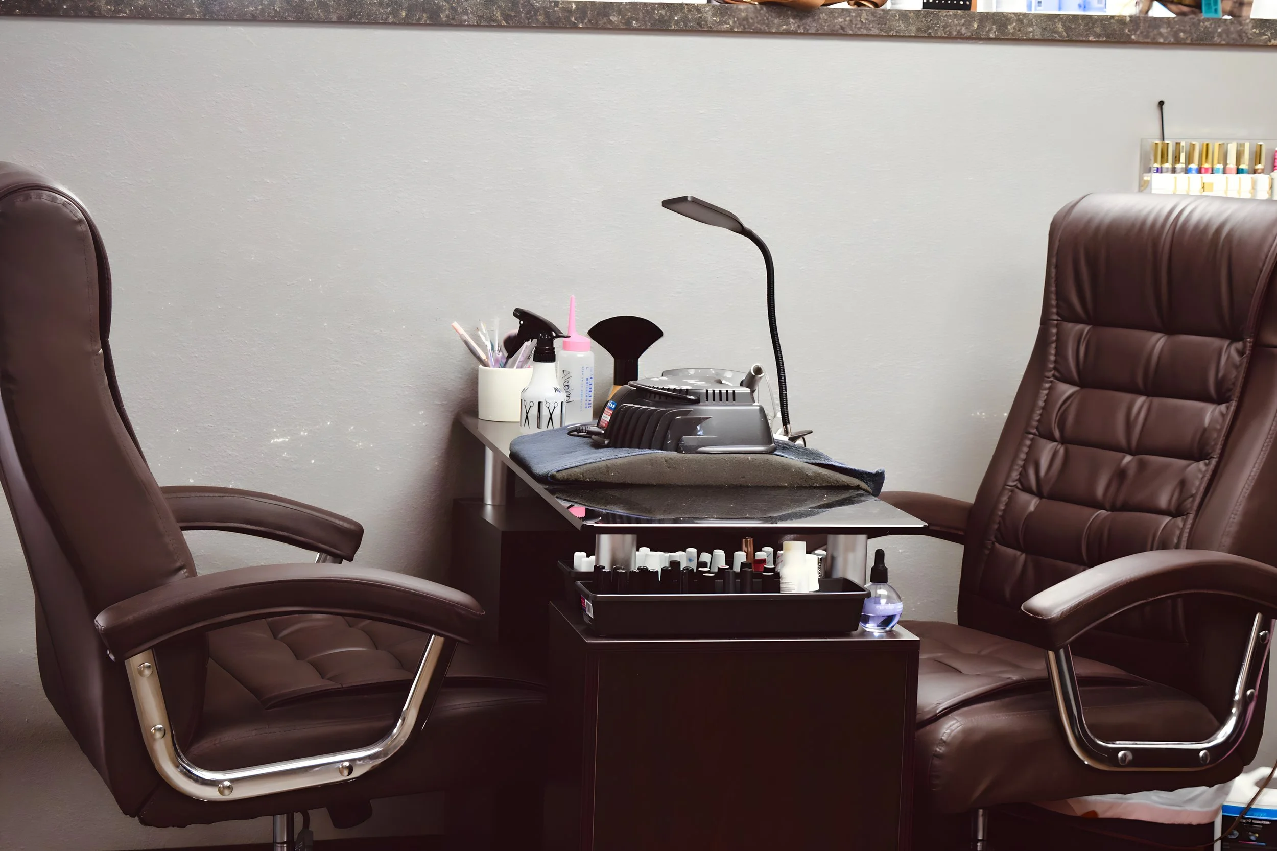 Office or workspace with two brown leather chairs, a small table with supplies including a lamp, nail polish bottles, and cleaning spray.