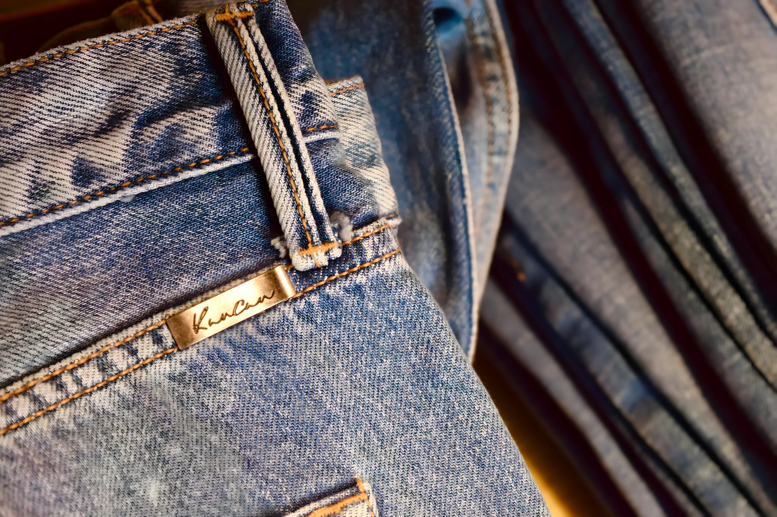Close-up of blue denim jeans with a gold brand tag reading 'Karan' near the waistband.