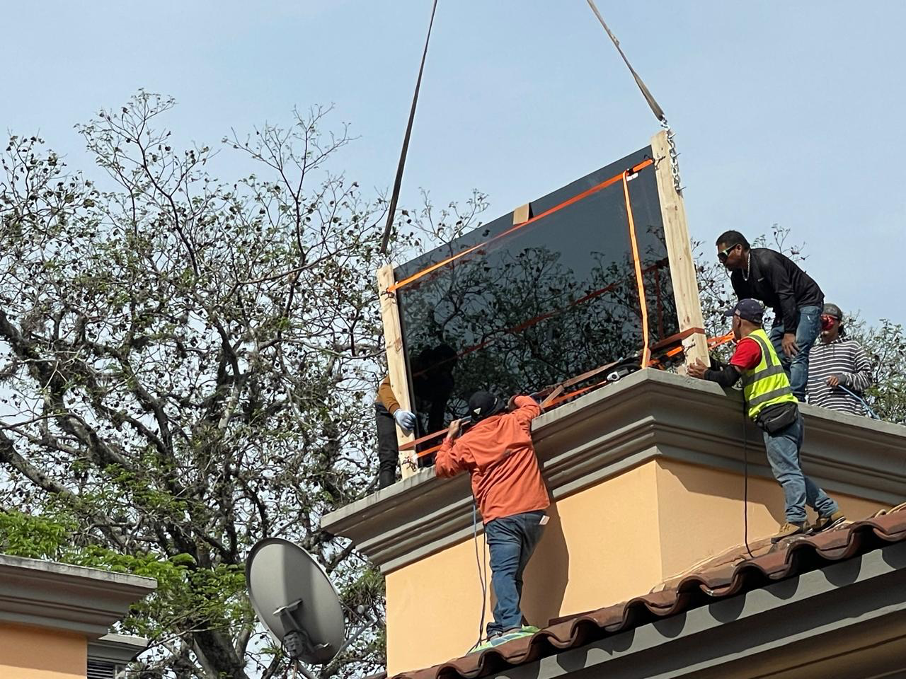 People installing a large, flat television on a rooftop ledge.