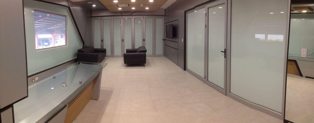 Interior of a modern waiting or lounge area with black leather chairs, large glass partitions, and a TV mounted on the wall.