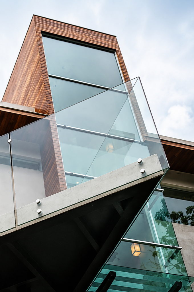 Modern building with wood and glass exterior, featuring large windows, glass balcony, and a staircase with glass balustrades.