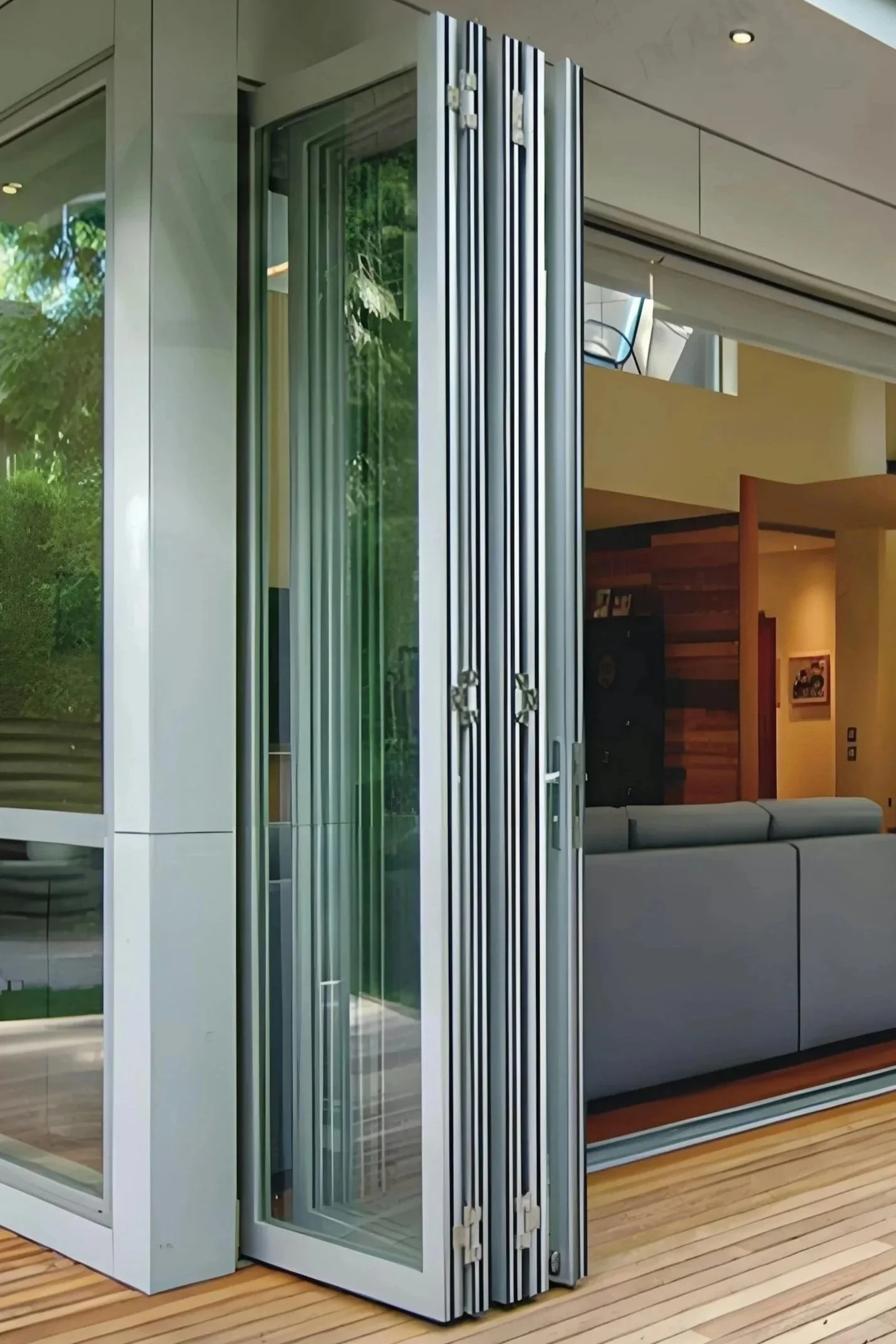 A set of large sliding glass windows with metal frames, partially open, revealing a modern interior with wood paneling and hardwood flooring.