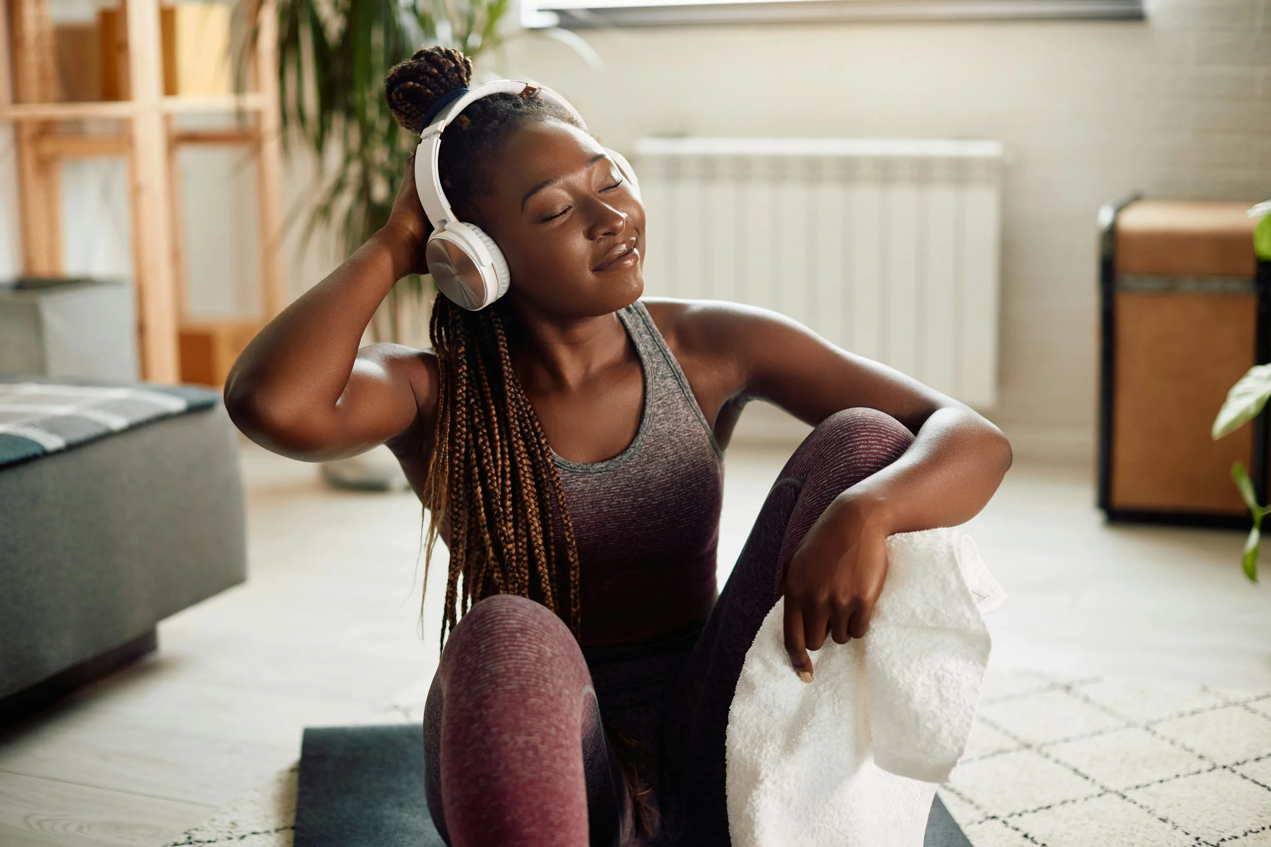 Woman sitting on floor at home with headphones on, eyes closed, at ease