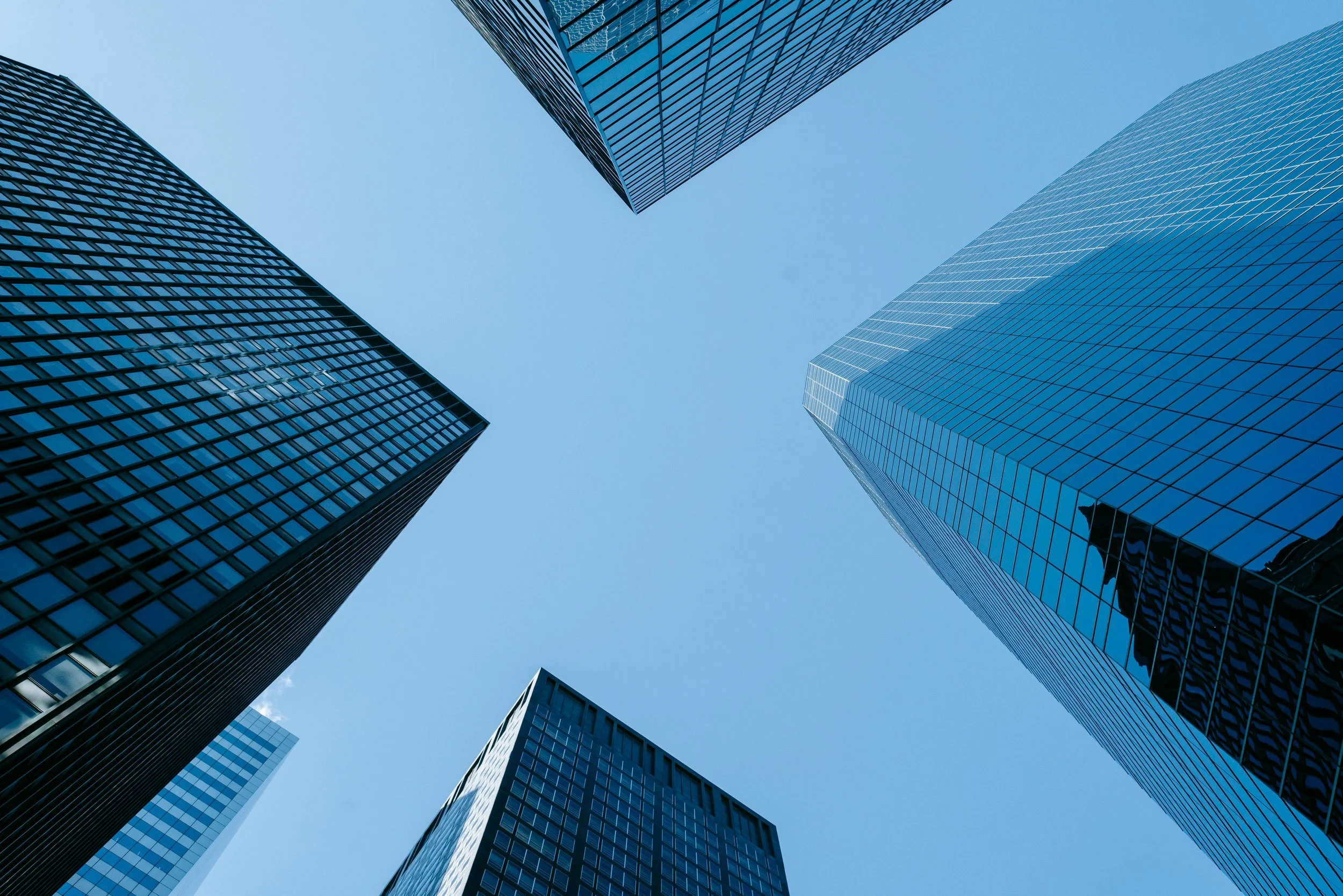 Looking up at tall glass skyscrapers against a clear blue sky.