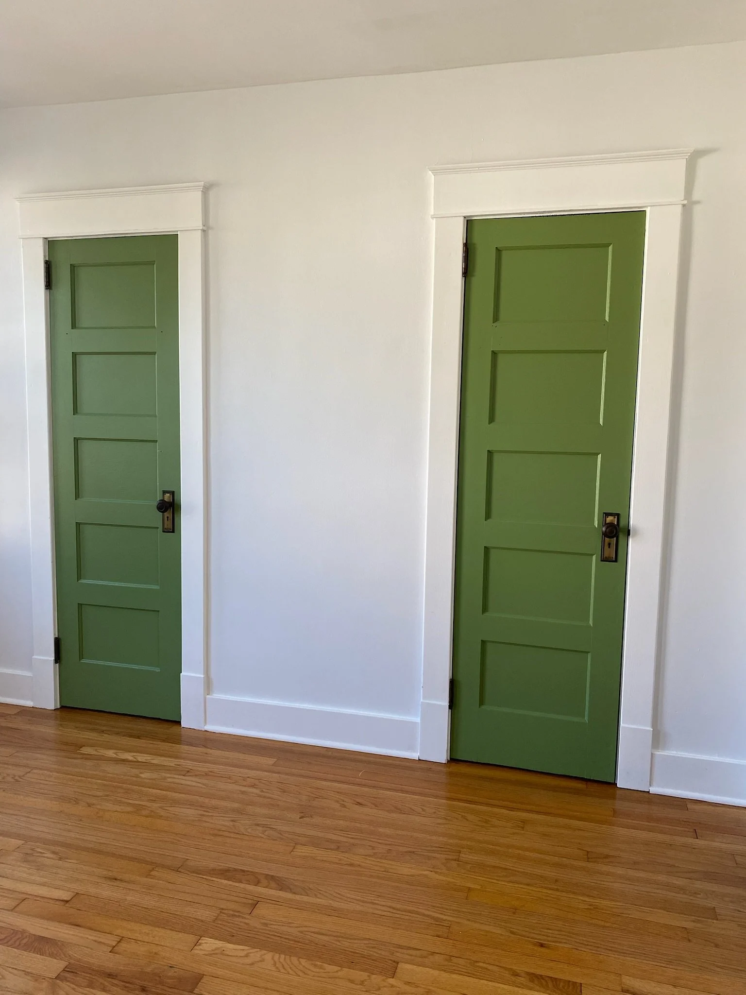 Pair of custom-painted interior paneled doors in a soft green finish with white trim, showcasing detailed finish carpentry, clean casing profiles, and restored hardwood flooring.