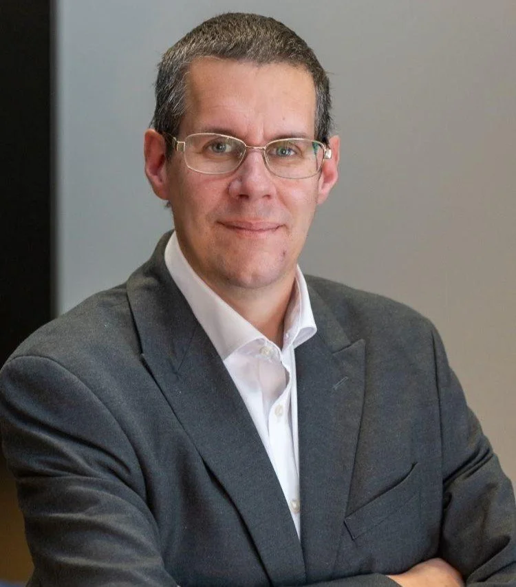 The image shows a man wearing glasses in a professional headshot.