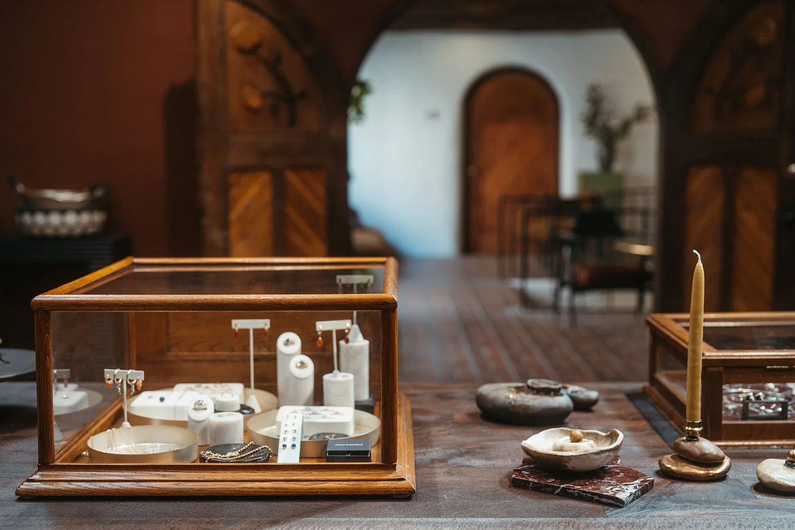 Display case containing jewelry, along with stones, candles, and decorative items on a wooden table in a cozy, rustic room.