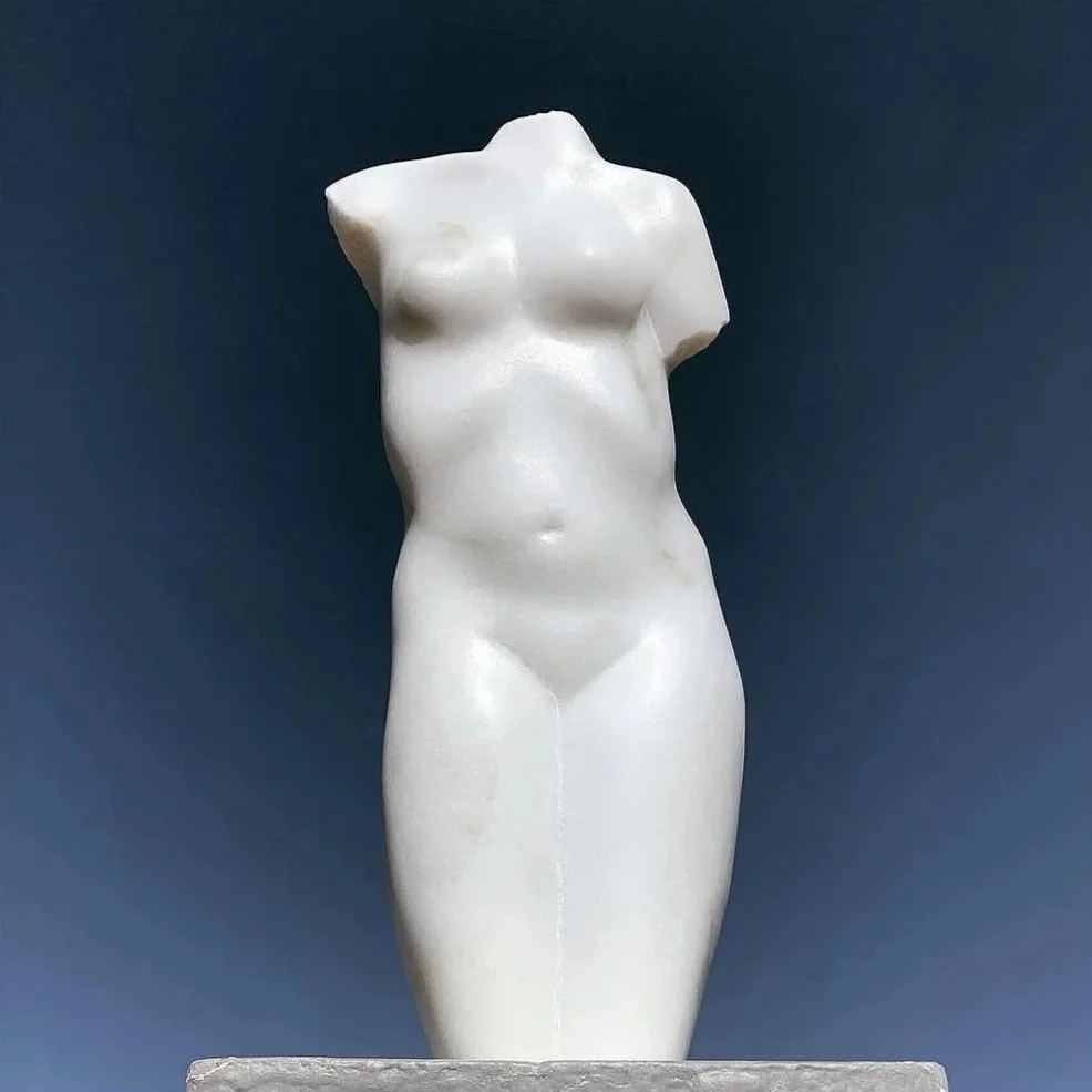 Marble sculpture of a female torso with missing head and arms against a dark background.