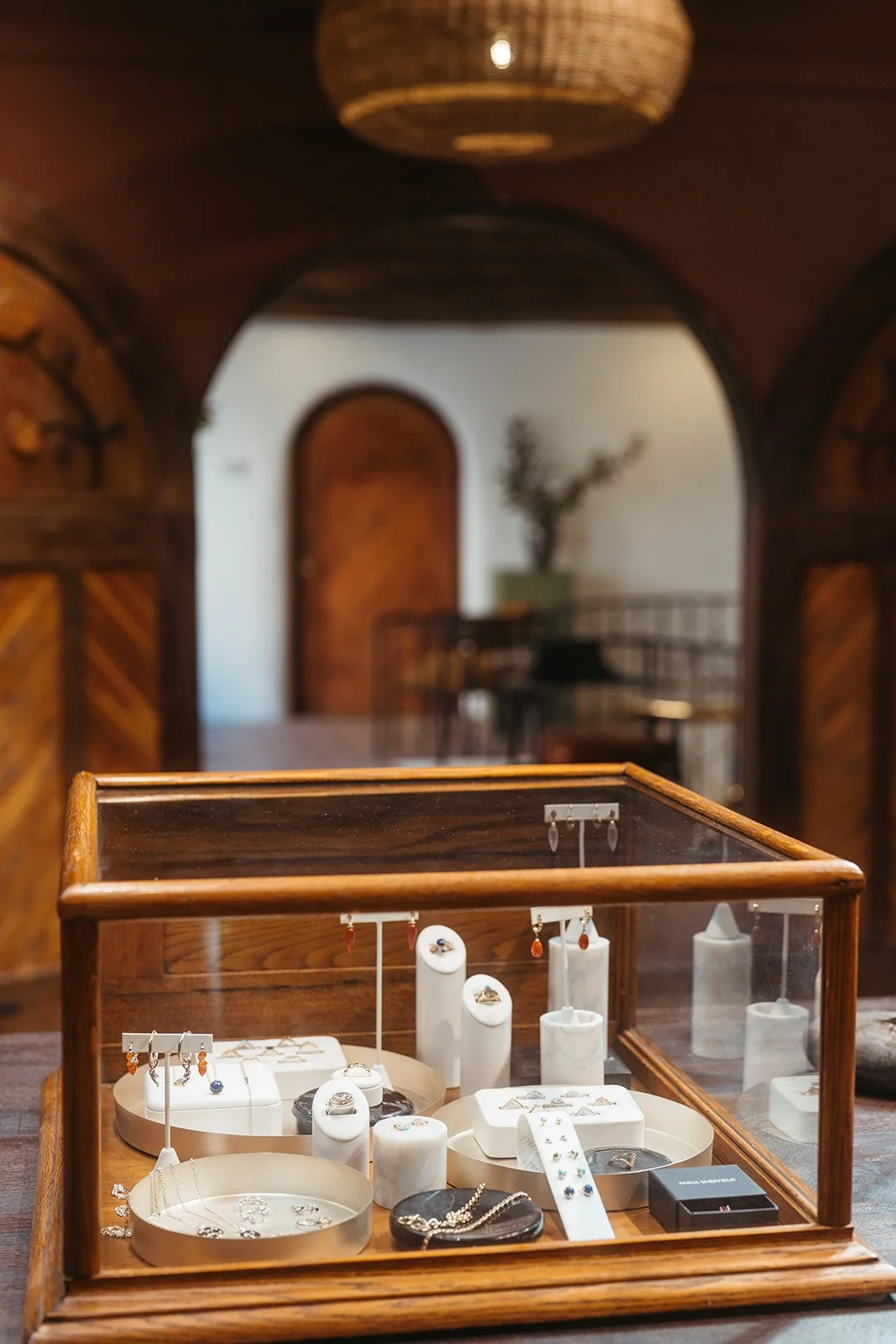 Display case with jewelry inside a wooden and glass enclosure, situated on a table in a warmly lit room with wooden walls and decorative elements.