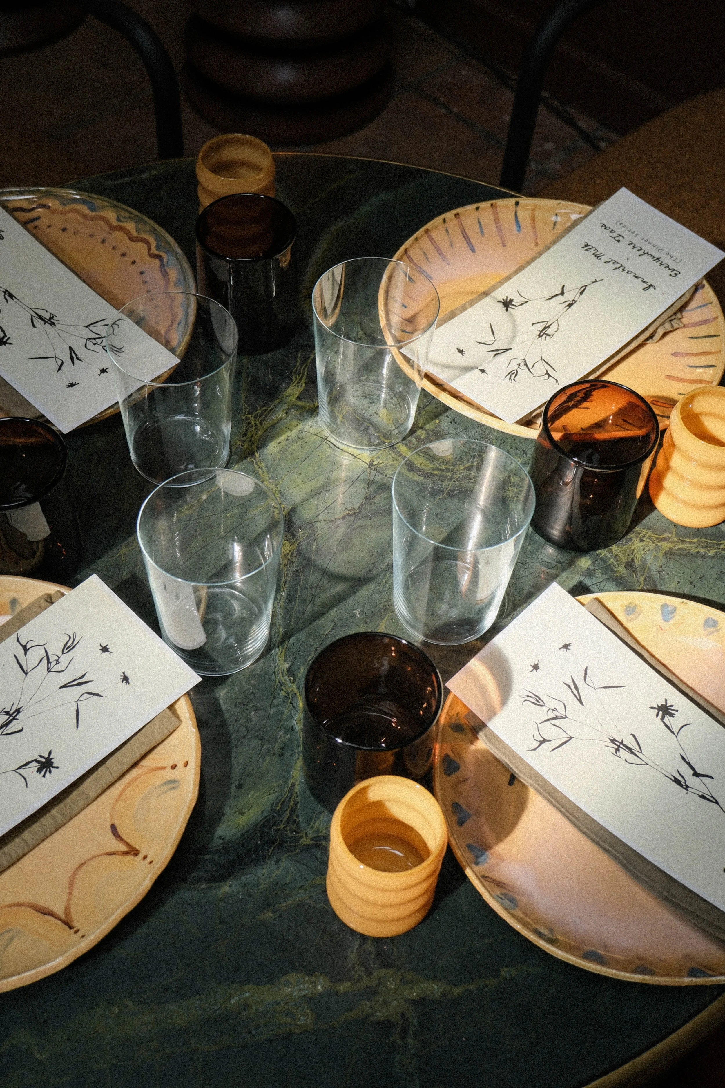 A round dining table set with ceramic plates, glass cups, and paper napkins with handwritten notes and floral drawings, in a cozy indoor setting.