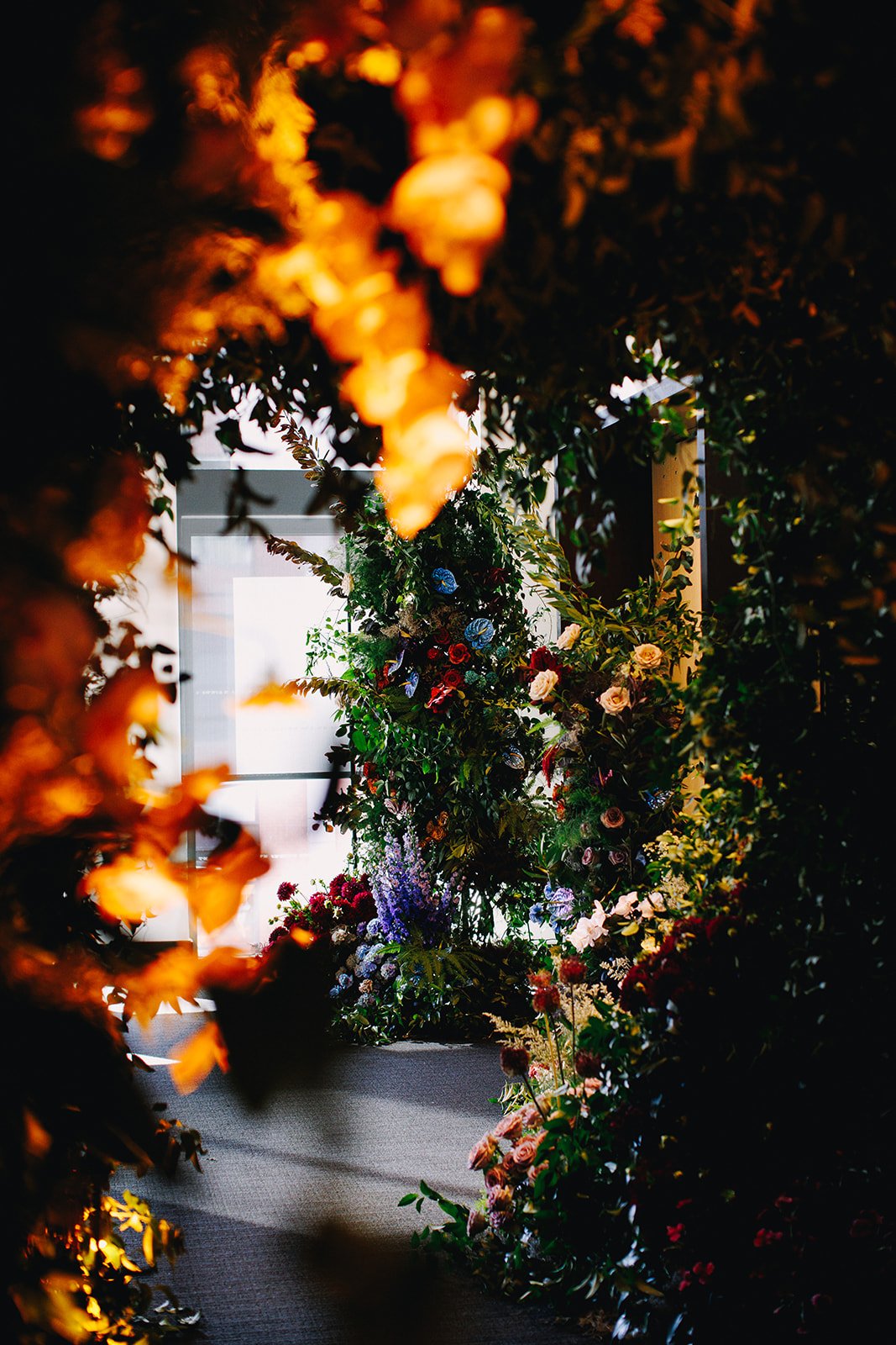 A pathway through a room decorated with elaborate floral arrangements, with a doorway in the background illuminated by natural light.