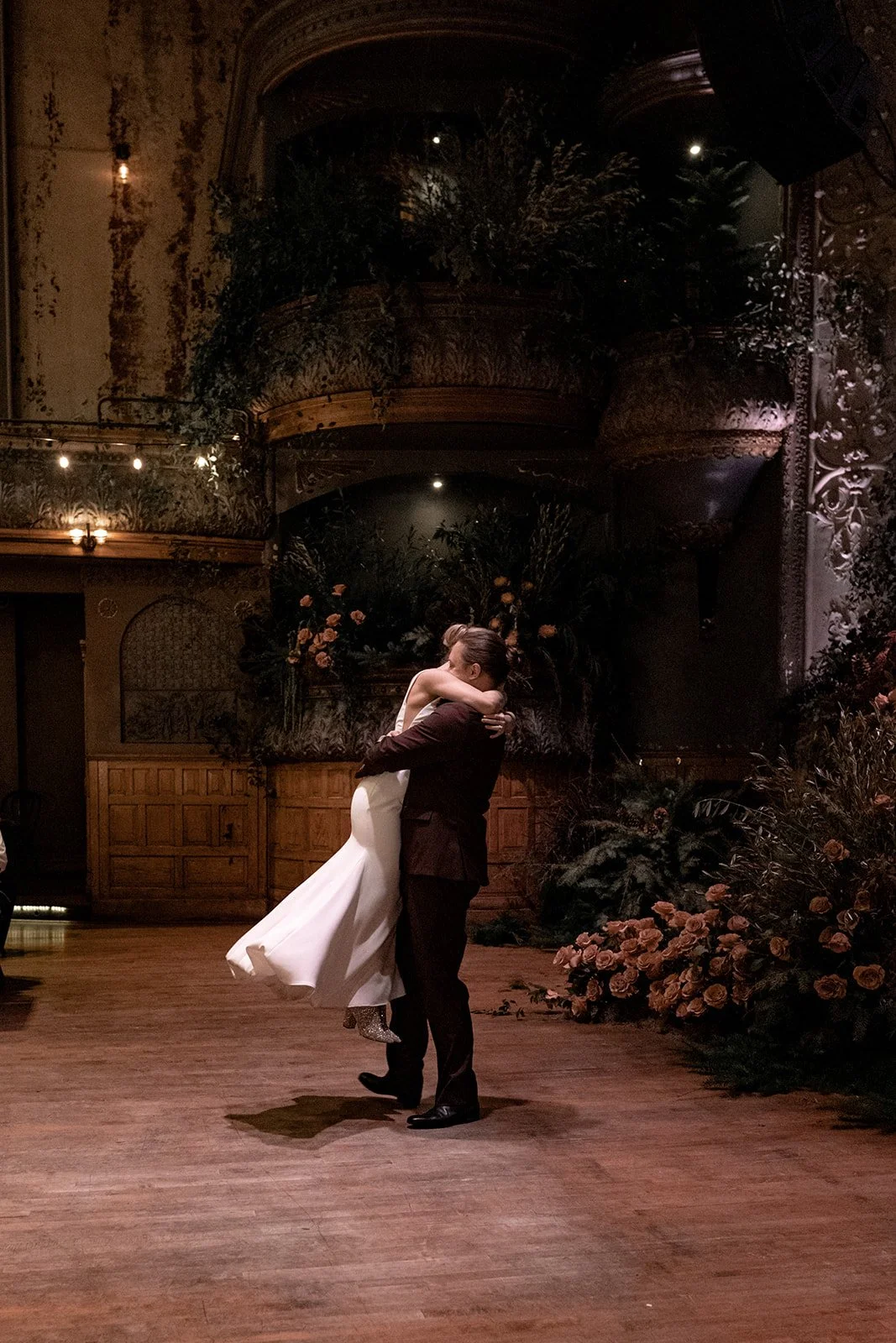A couple dancing closely in an elegant, dimly lit venue decorated with flowers and greenery.