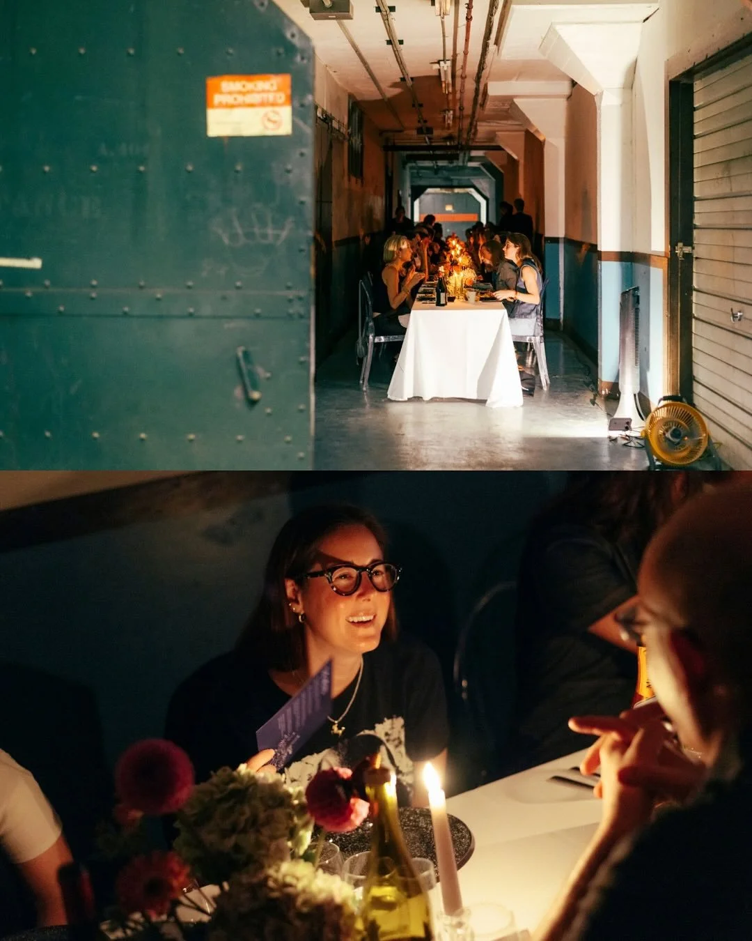 A dinner party in an industrial-style venue with a long table, people dining, and a woman smiling and conversing in a cozy, dimly-lit setting with flowers and a candle.
