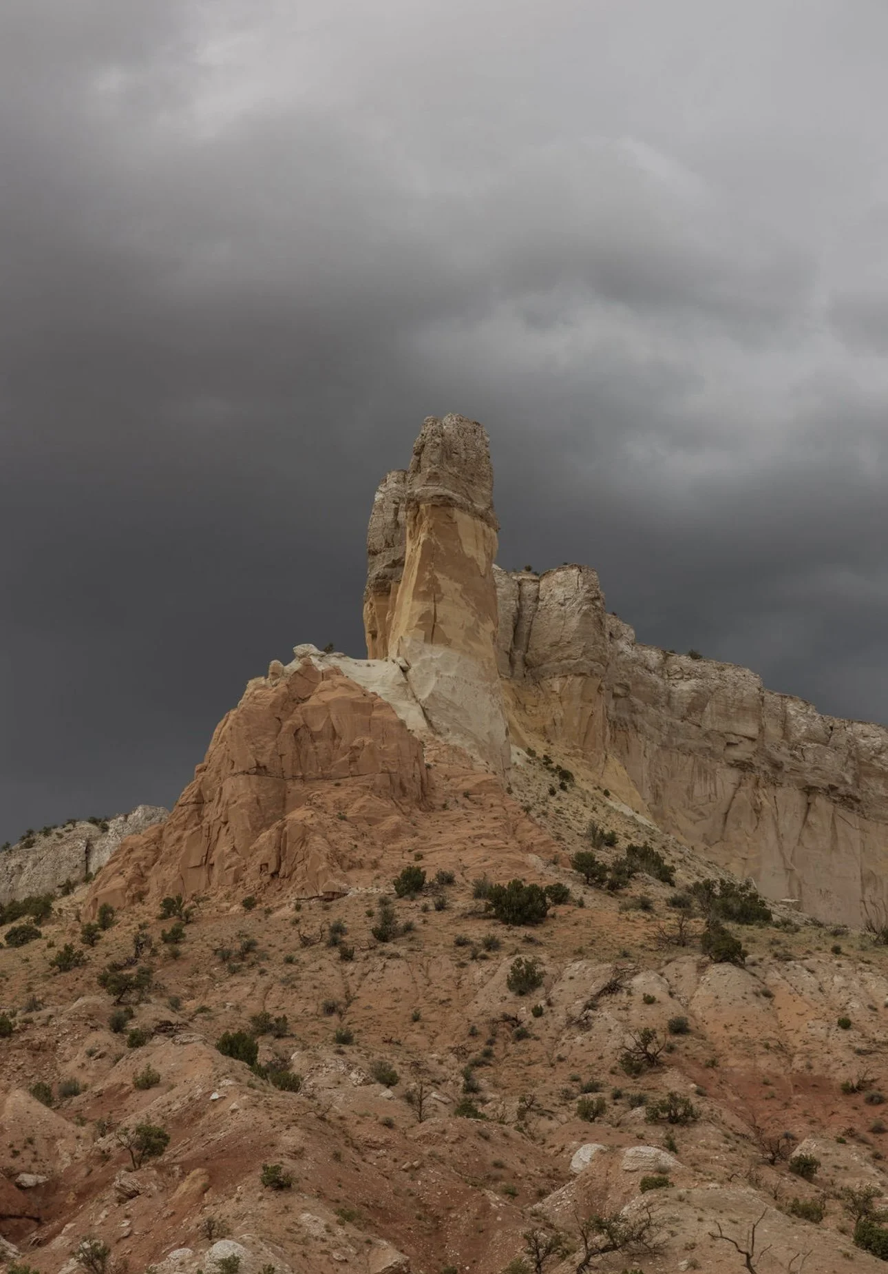 Dark storm clouds over rugged desert rock formations with sparse vegetation.