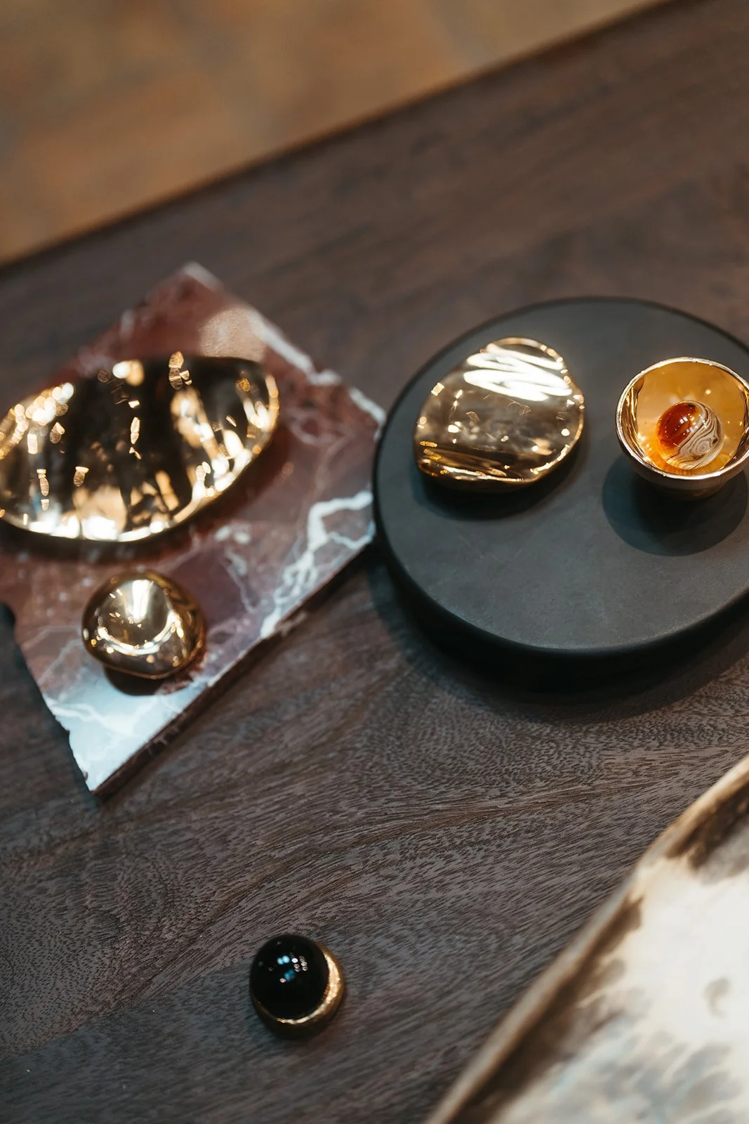 Decorative gold and black polished stones and objects on black and marble plates on a dark wooden surface.