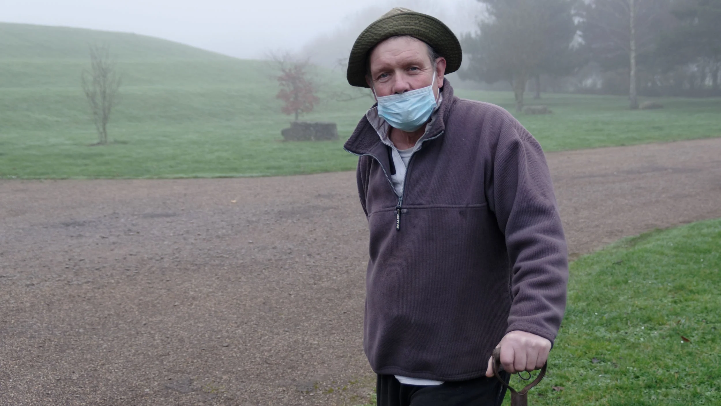 A gardener wears a Covid mask in a misty local park.