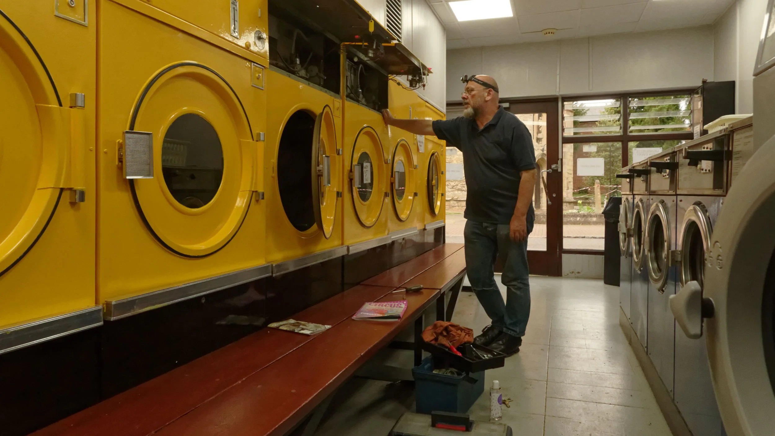 Self portrait repairing yellow painted Hoebsch dryer, in closed for evening launderette