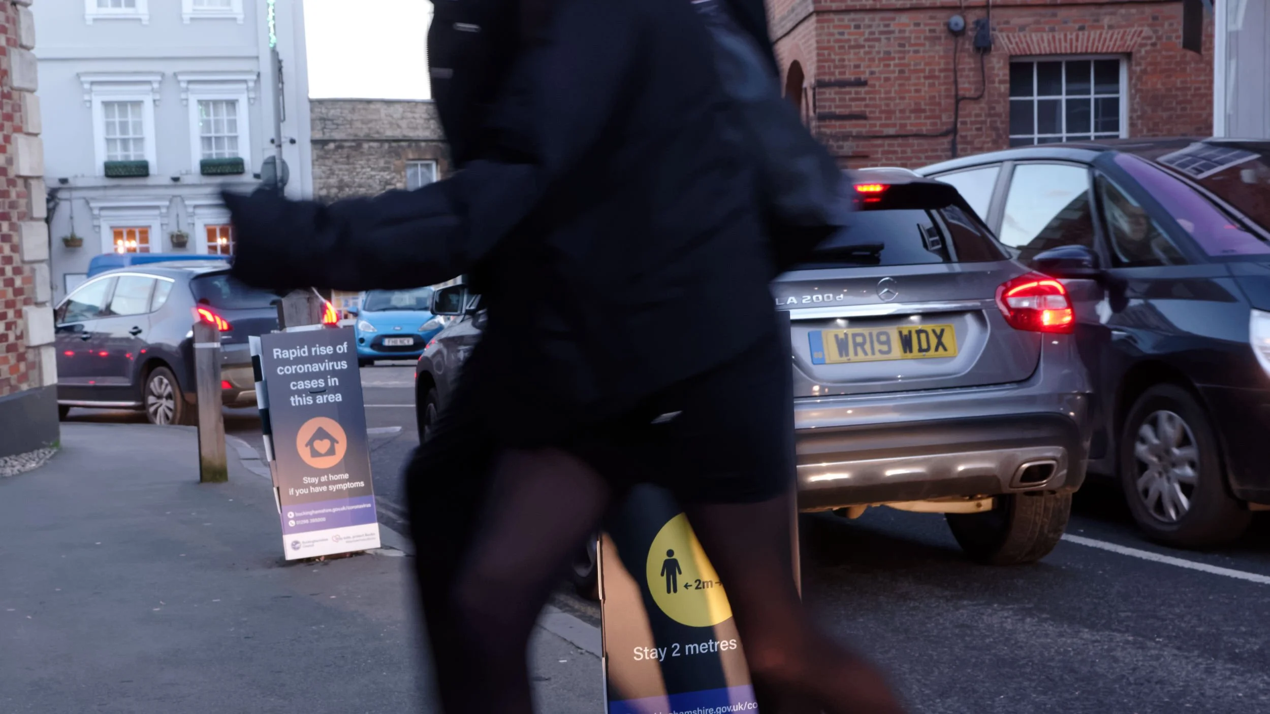 Covid warning signs on narrow pavement and one pedestrian in Buckingham, Bucks.