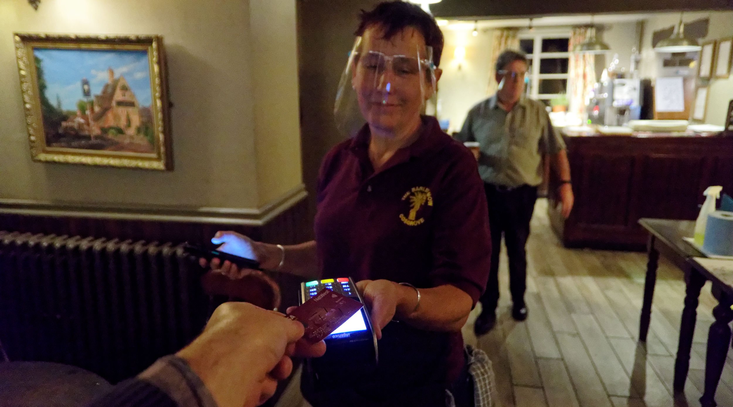 Paying for my drink in the pub. Staff wear Covid face shields.