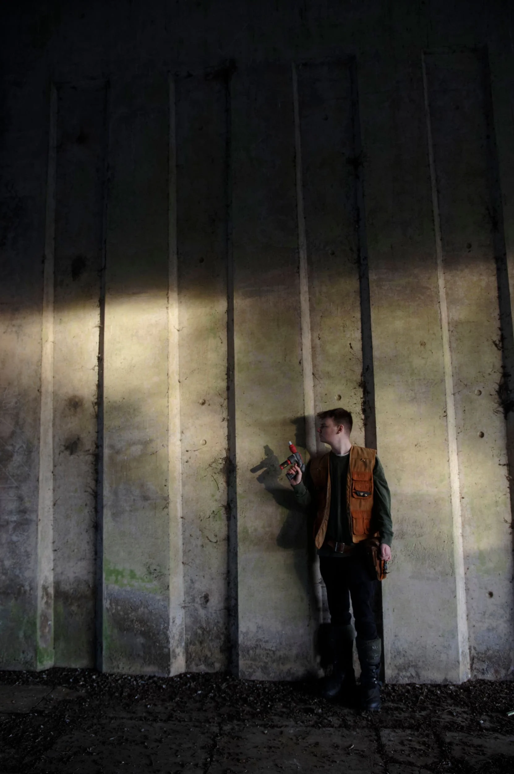 Man with blaster weapon stands ready, looking along a concrete wall.
