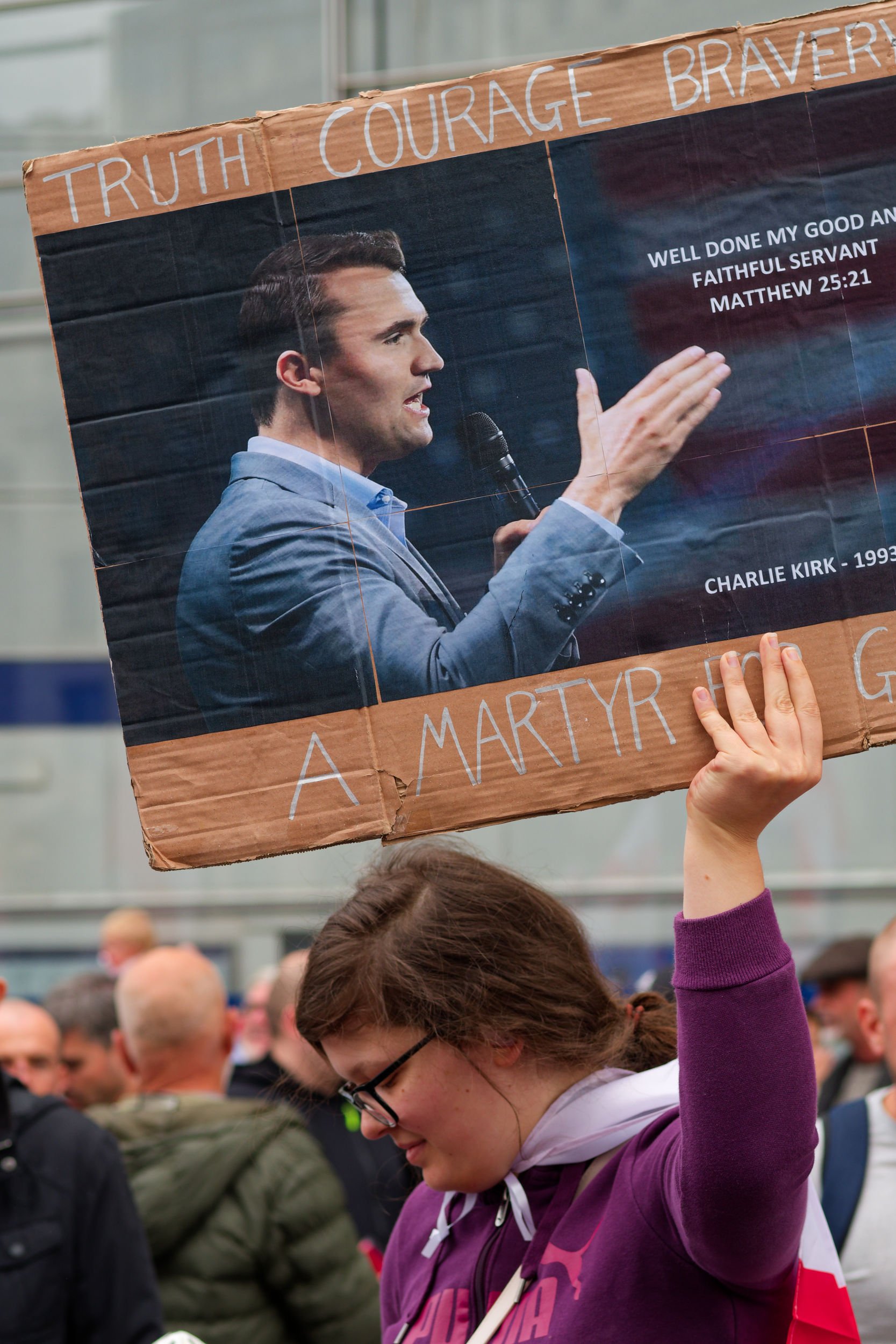 Woman holds Charlie Kirk sign at Tommy Robinson's Unite the Kingdom rally.