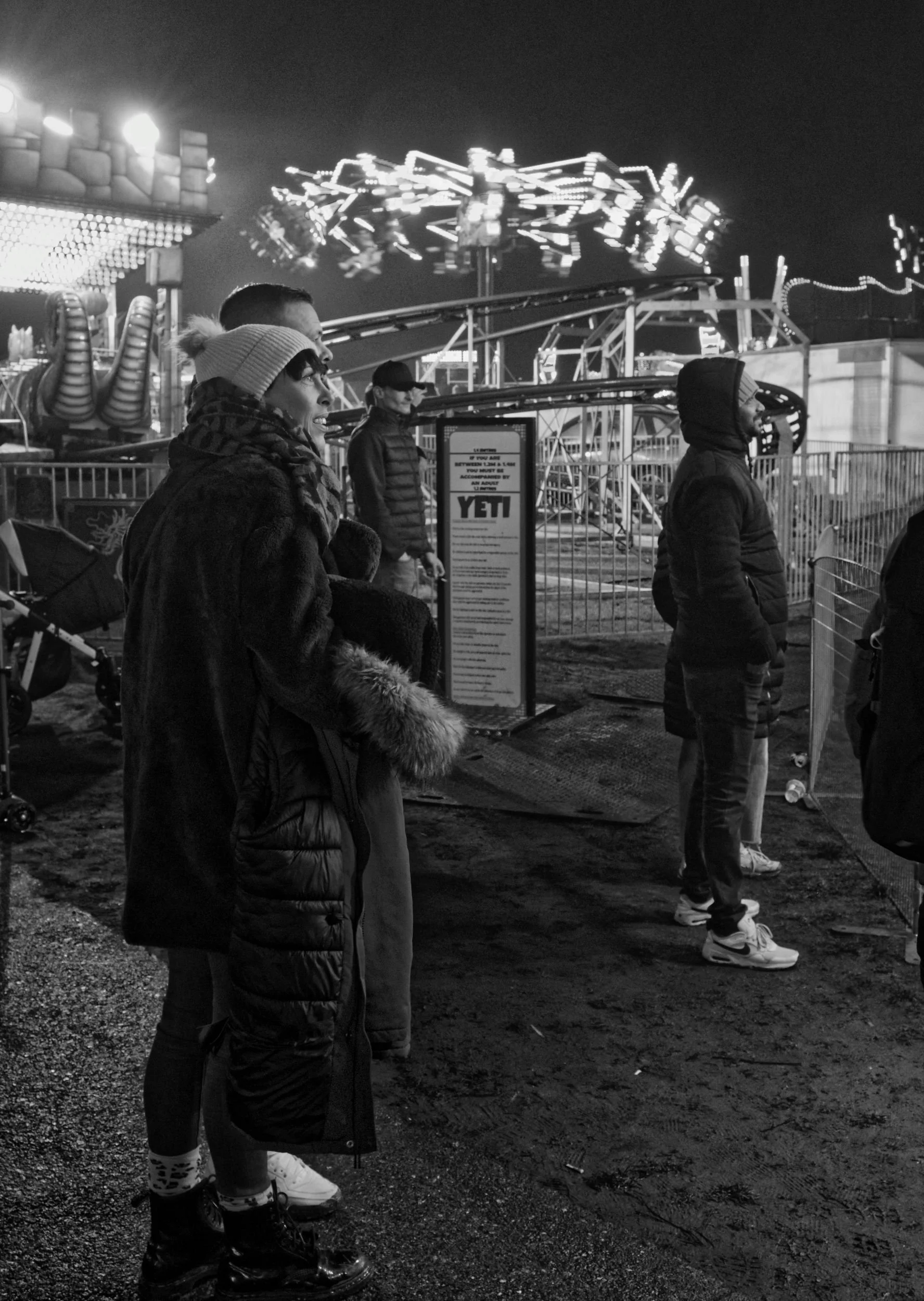 Adults watch a fairground ride. A black and white photo.