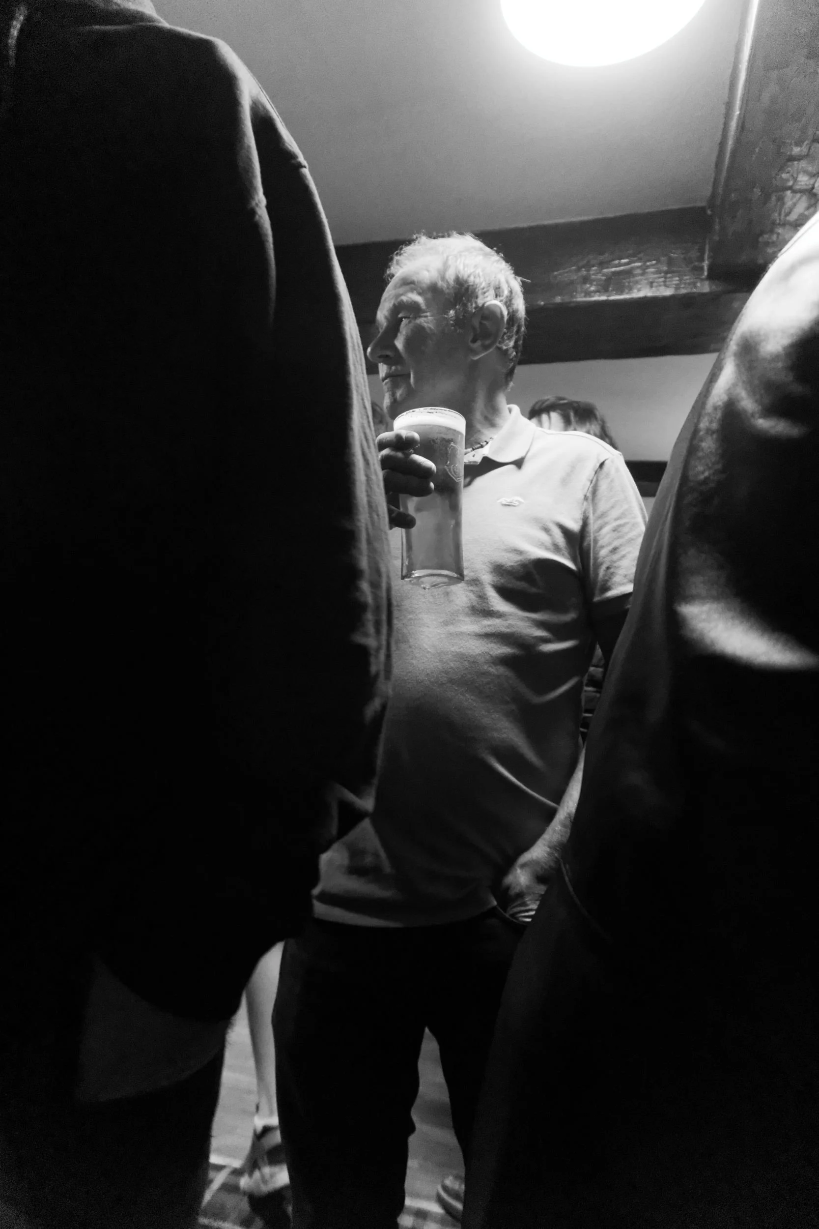 Man in crowded pub holding a pint of beer. Monochrome photo.