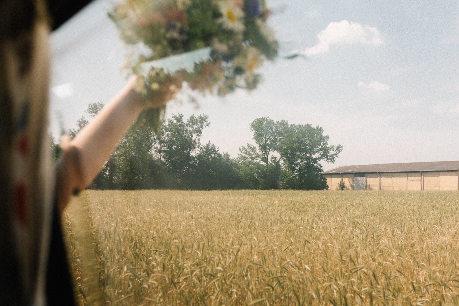 Blick aus Auto durch Scheibe, Kornfeld, Arm aus Fenster mit Brautstrauß