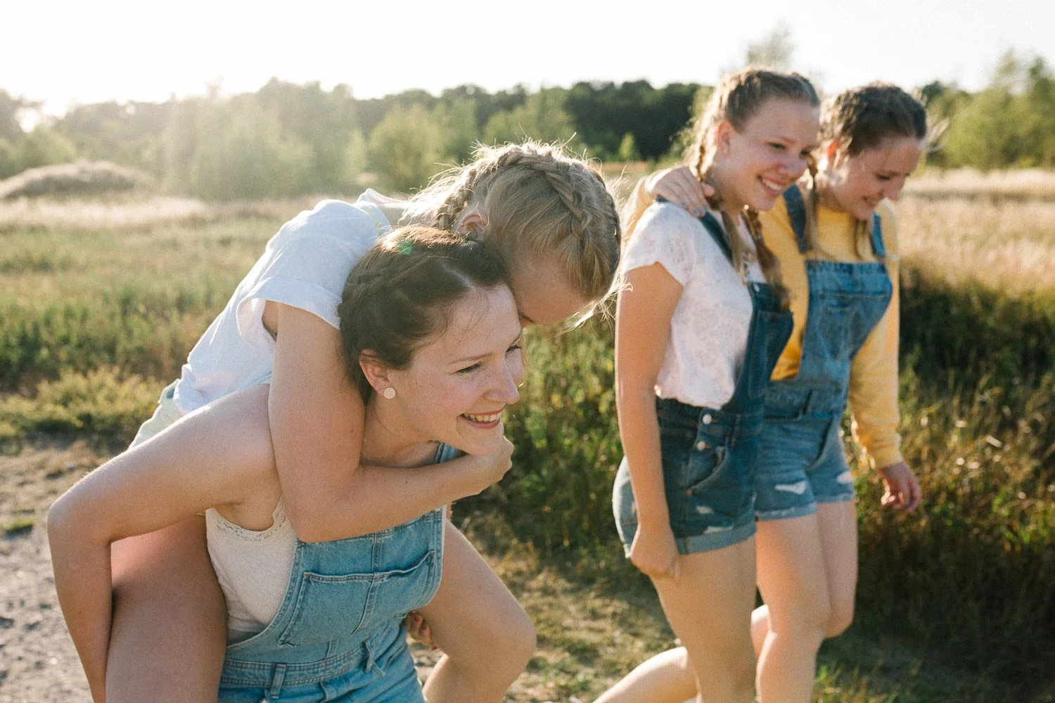 Schwestern laufen Arm in Arm und Huckepack Sommertag Sonnenlicht im Hintergrund