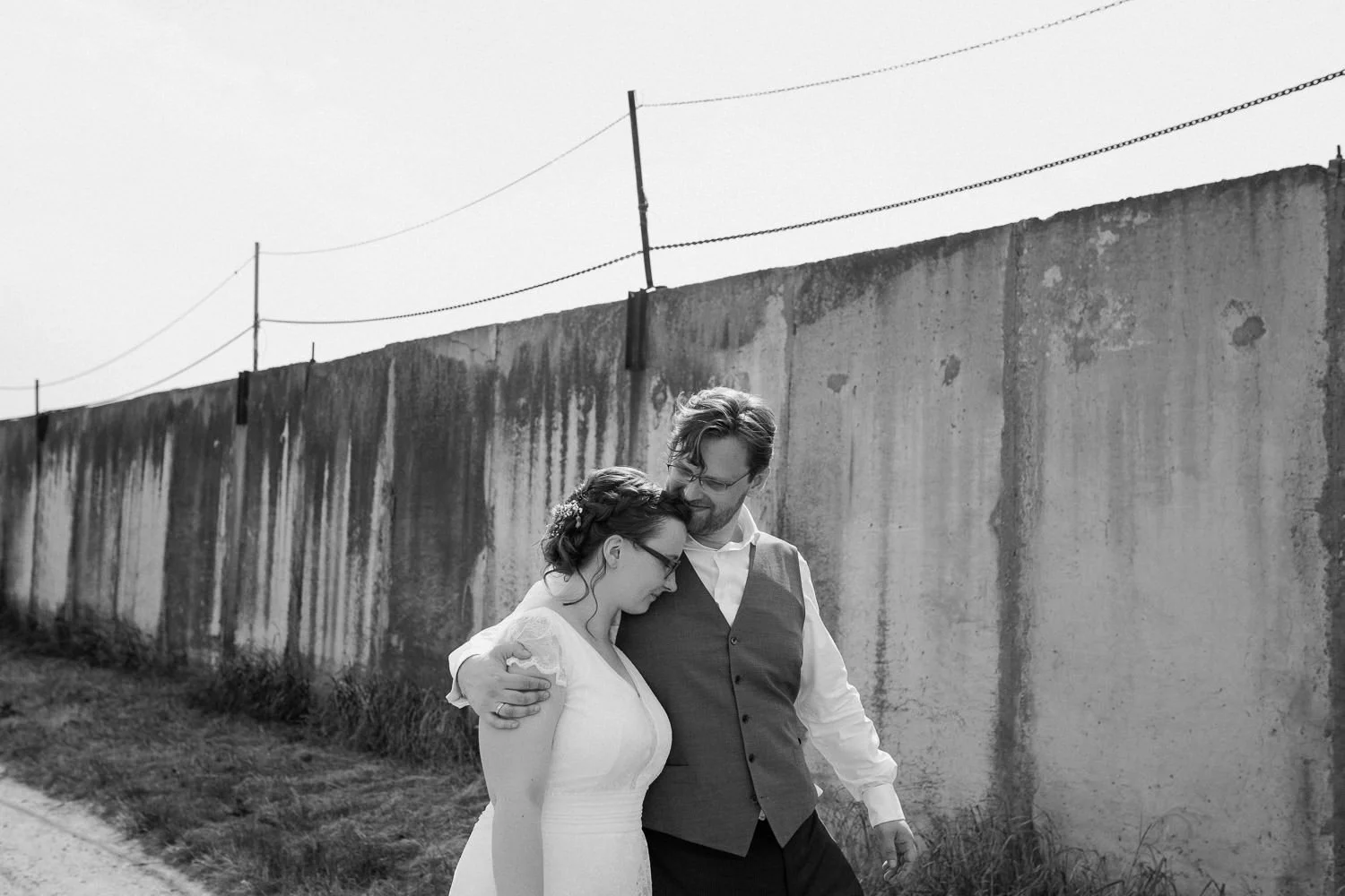 Brautpaar läuft Feldweg entlang, Mauer im Hintergrund, Schwarzweiß Foto